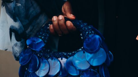 Close-up of a blue circular handbag held by a person with colorful attire, stylish and artistic.