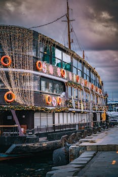 A beautifully decorated boat with festive lights docked by the pier under a moody sky.