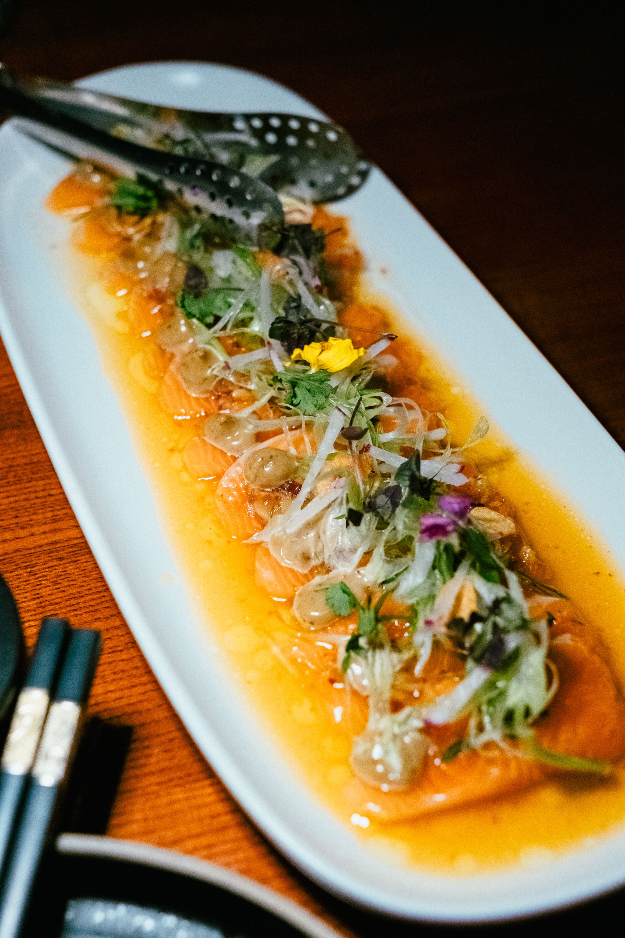 A vibrant platter of Asian-style salmon sashimi garnished with fresh herbs in a restaurant setting.