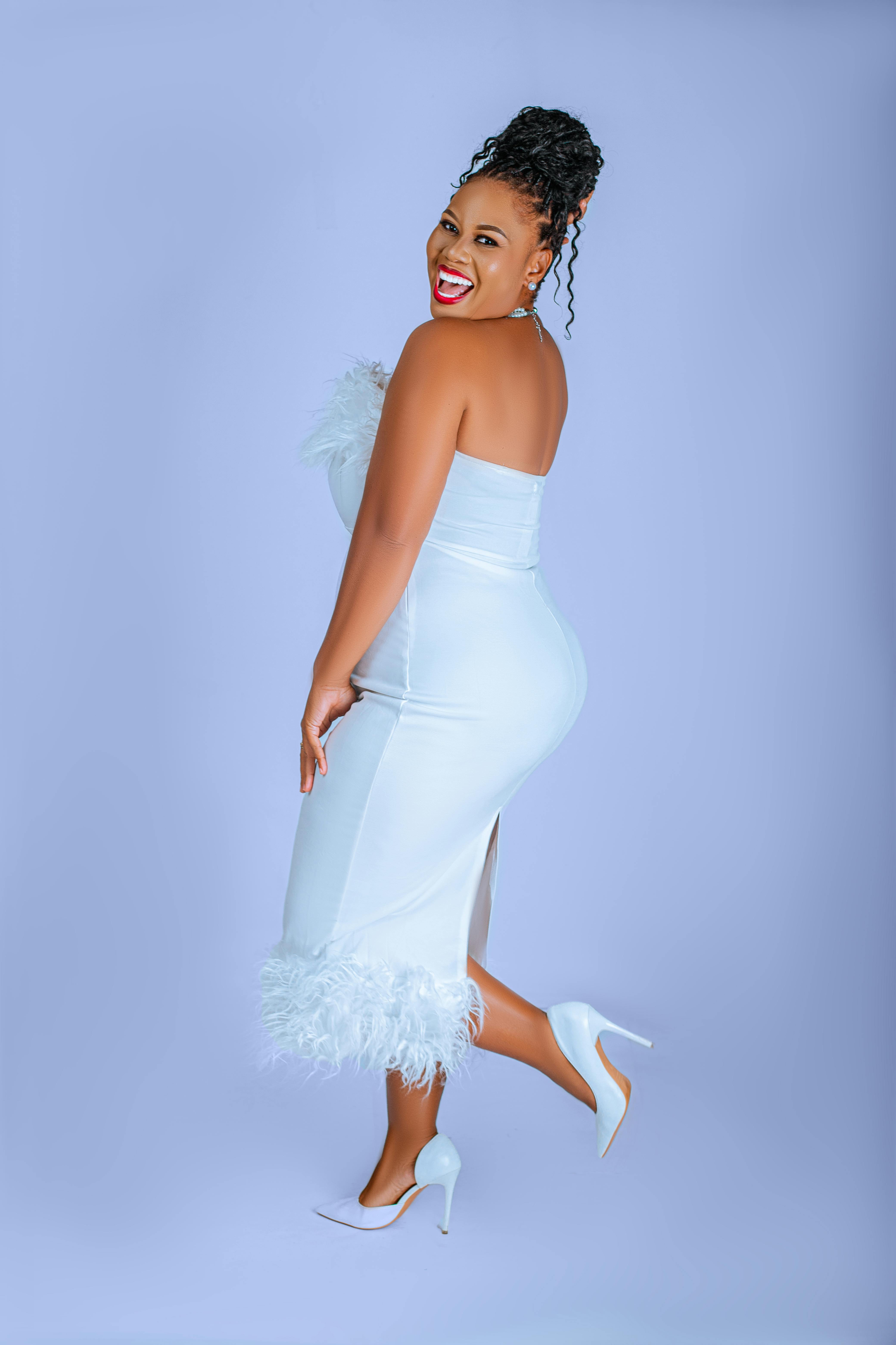 De franc Una dona elegant amb un vestit blanc de plomes posa juganerament sobre un fons blau pastel. Foto d'estoc