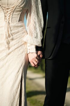 Close-up of a couple holding hands, showcasing wedding attire and rings. A symbol of love and commitment.