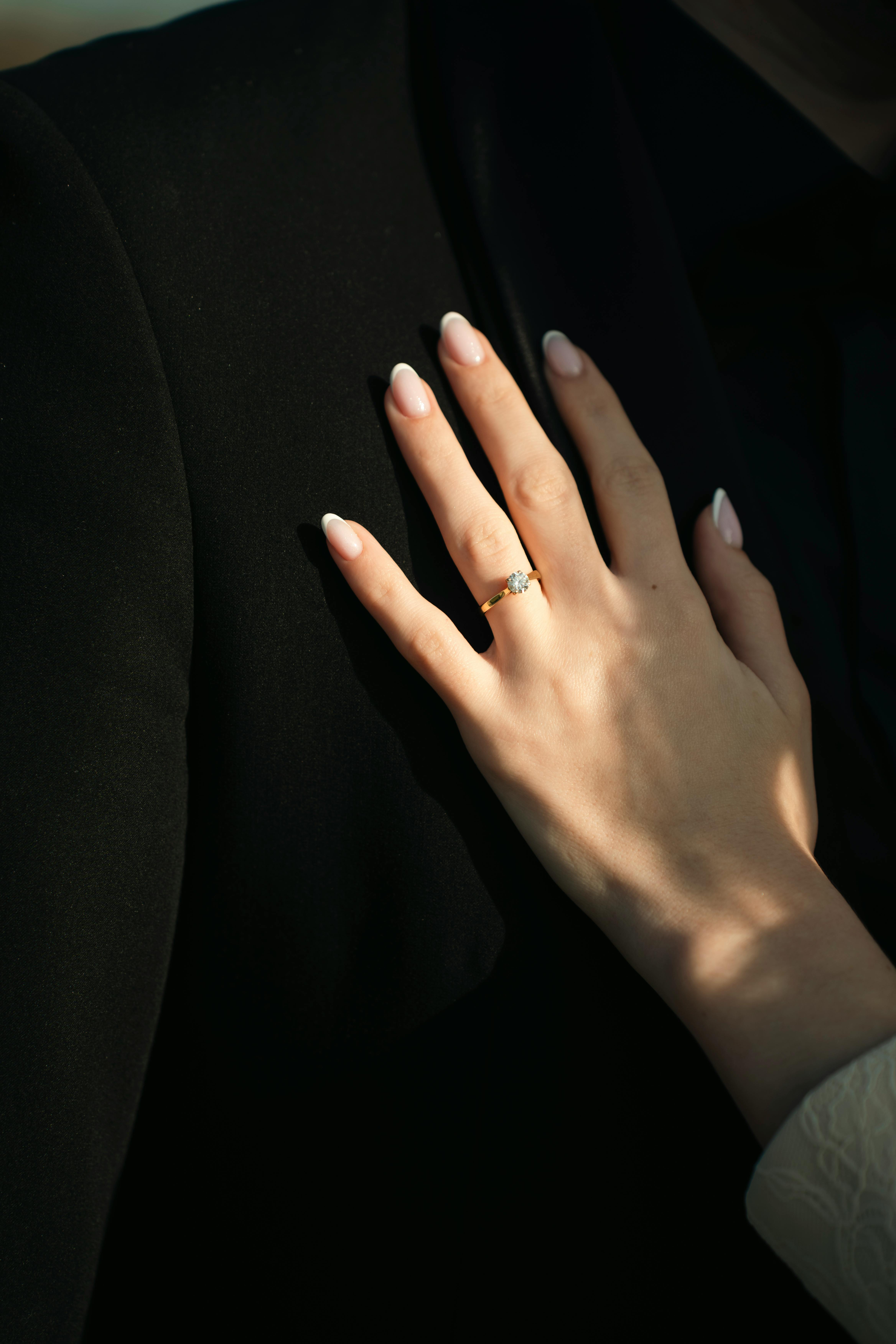 Gratis Primer plano de una mano elegante con un anillo de compromiso apoyado en un traje negro, simbolizando el amor y el compromiso. Foto de stock