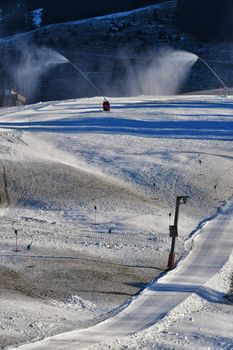 Snow machines creating artificial snow on ski slopes in a winter resort.