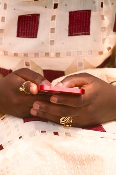 Close-up of hands holding a red smartphone, wearing gold rings.