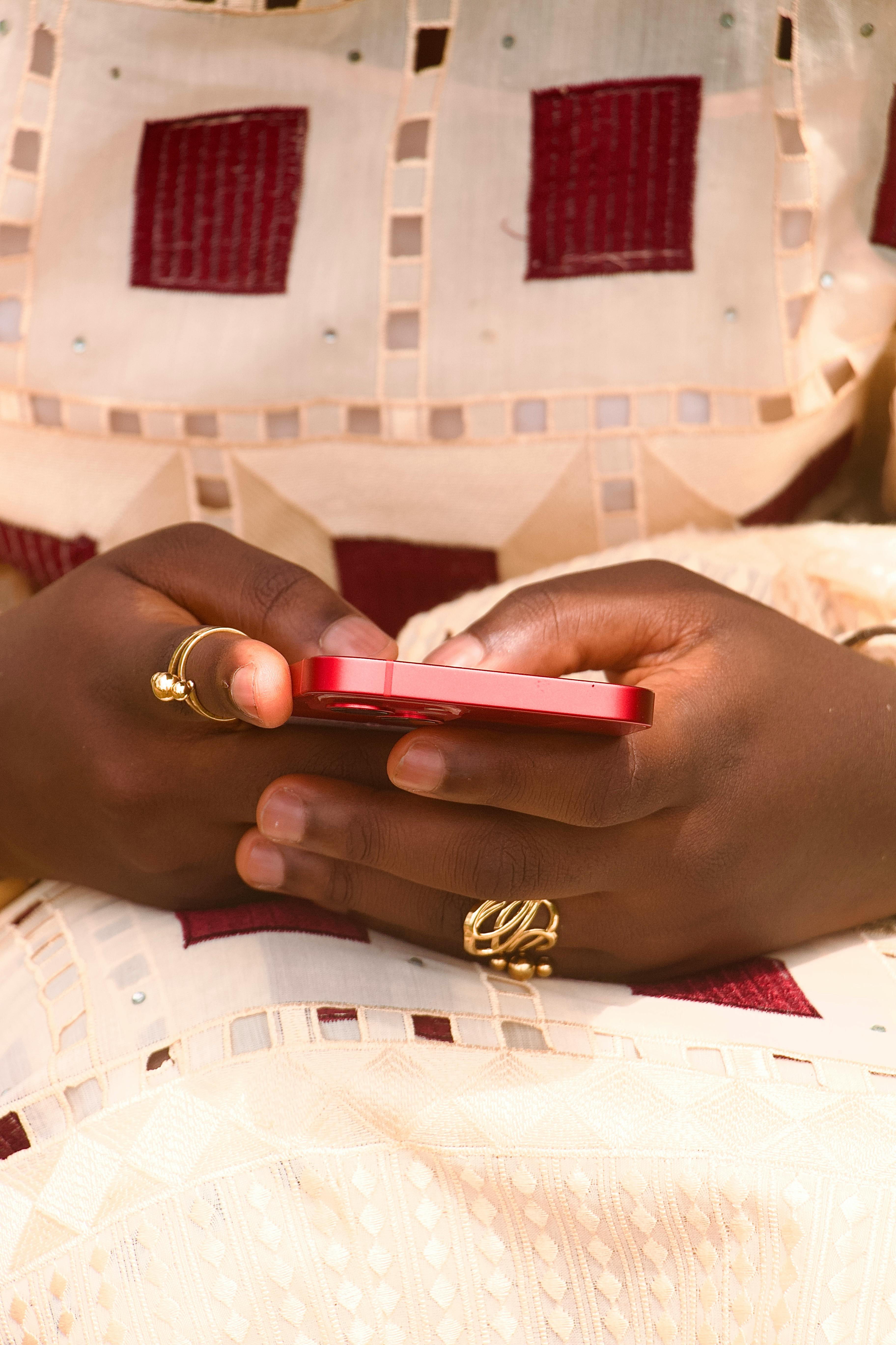 De franc Primer pla de mans que sostenen un telèfon intel·ligent vermell i porten anells daurats. Foto d'estoc