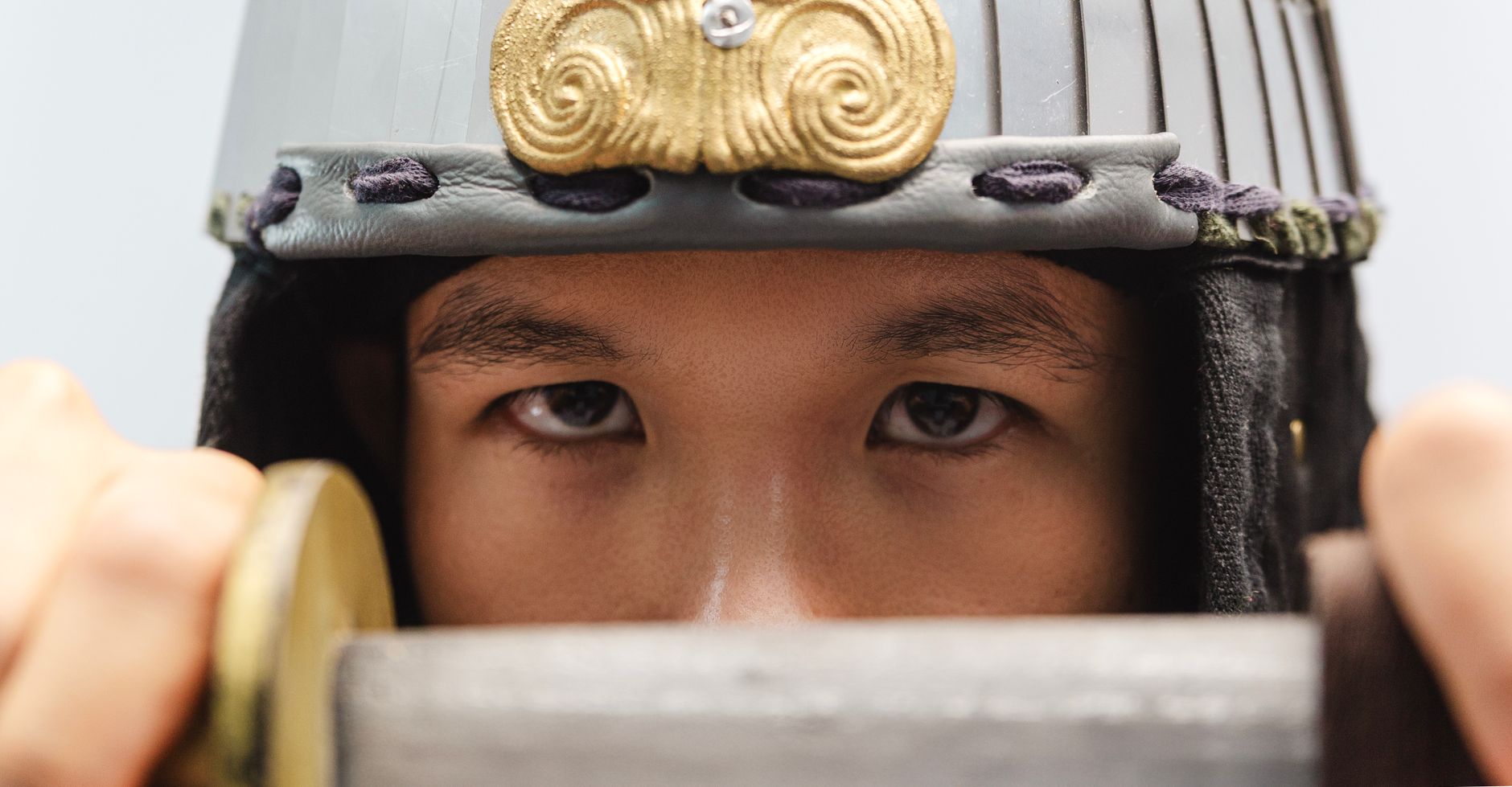 Close-up of a samurai warrior's eyes with a traditional helmet, holding a sword.