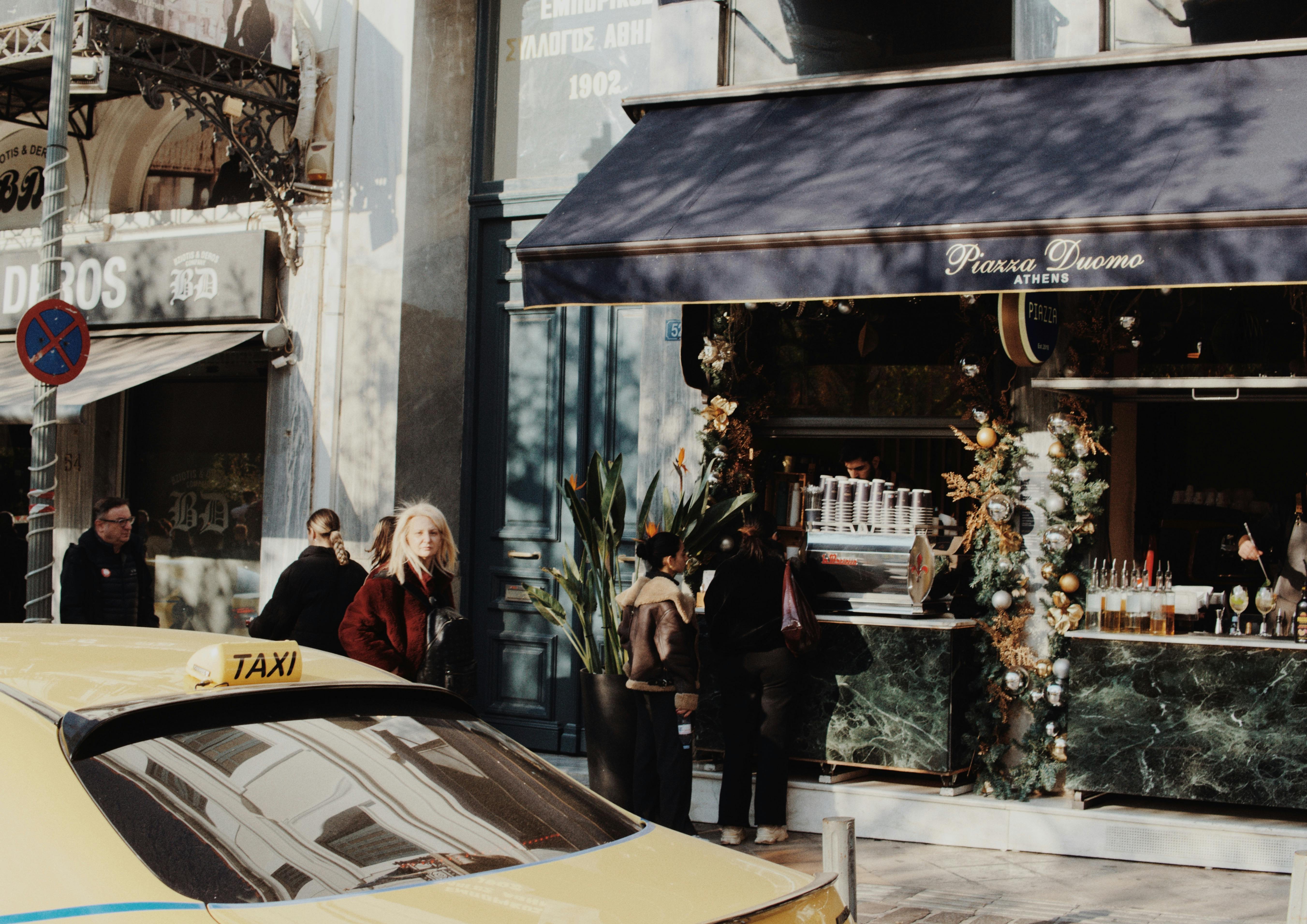 A vibrant street scene outside Piazza Duomo cafe with a taxi and decorations in Athens.