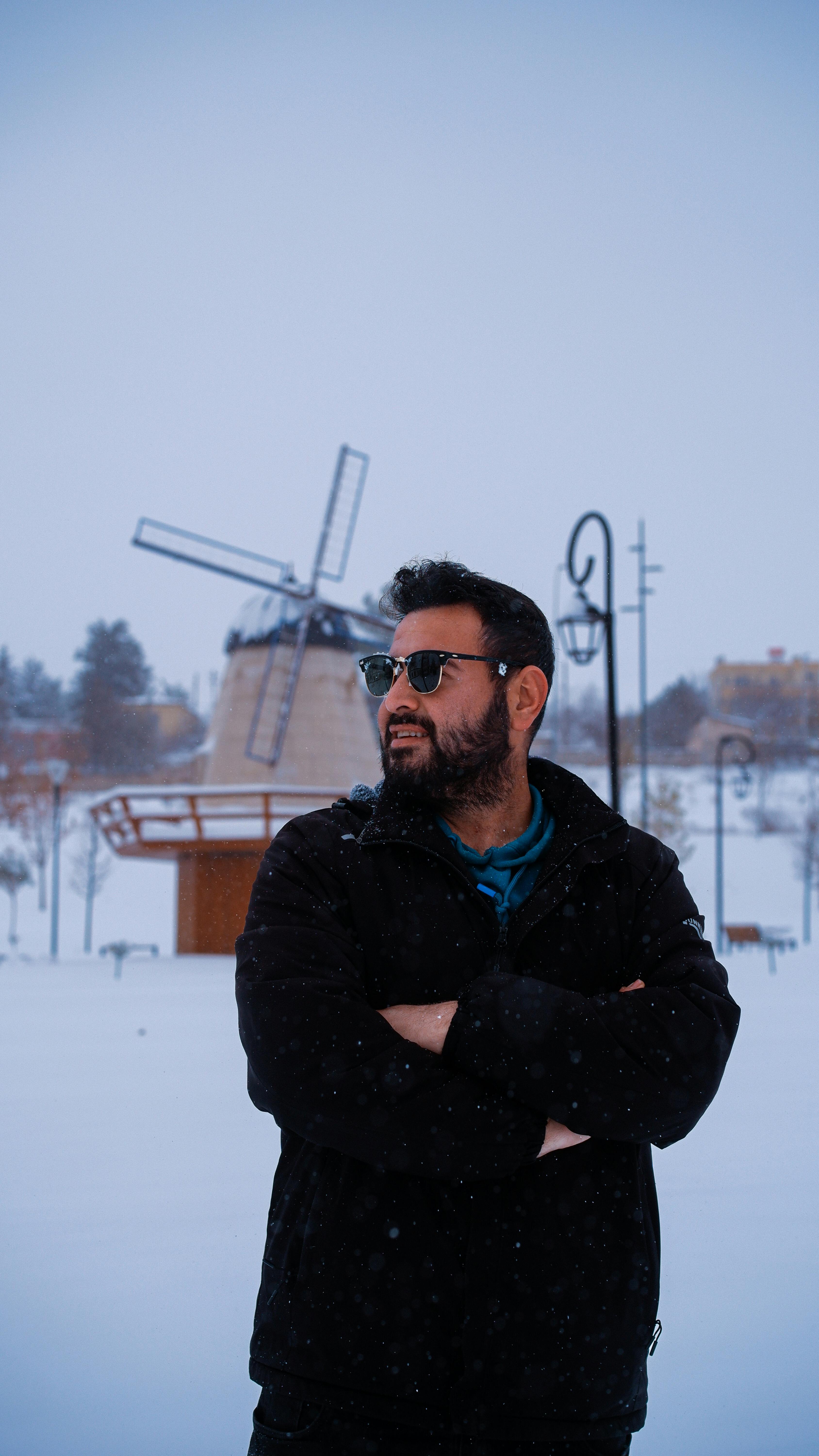 De franc Home amb ulleres de sol dempeus en un paisatge nevat amb un molí de vent al fons. Foto d'estoc