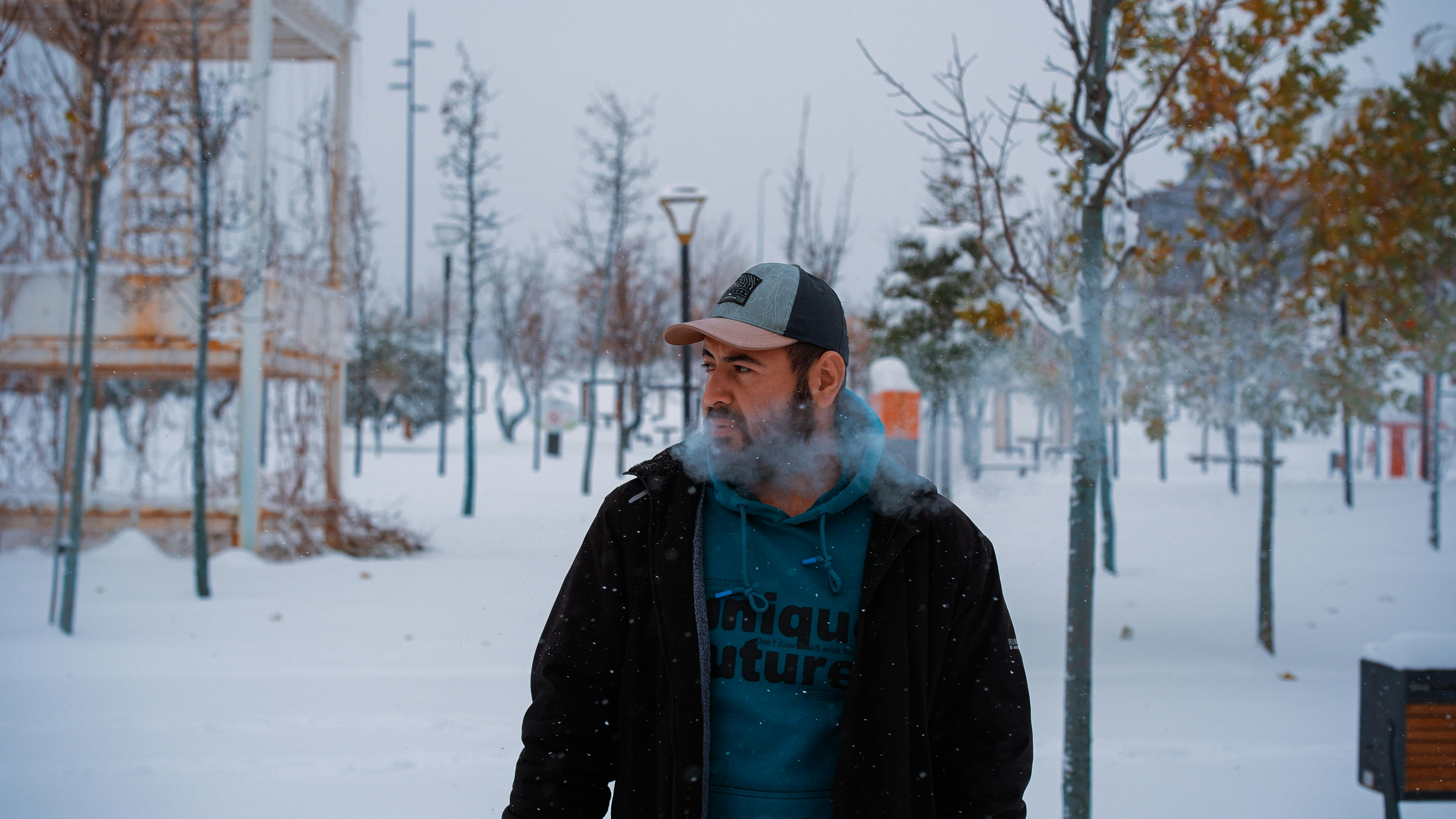 De franc Un home amb roba d'hivern exhala vapor en un dia de neu en un parc. Foto d'estoc