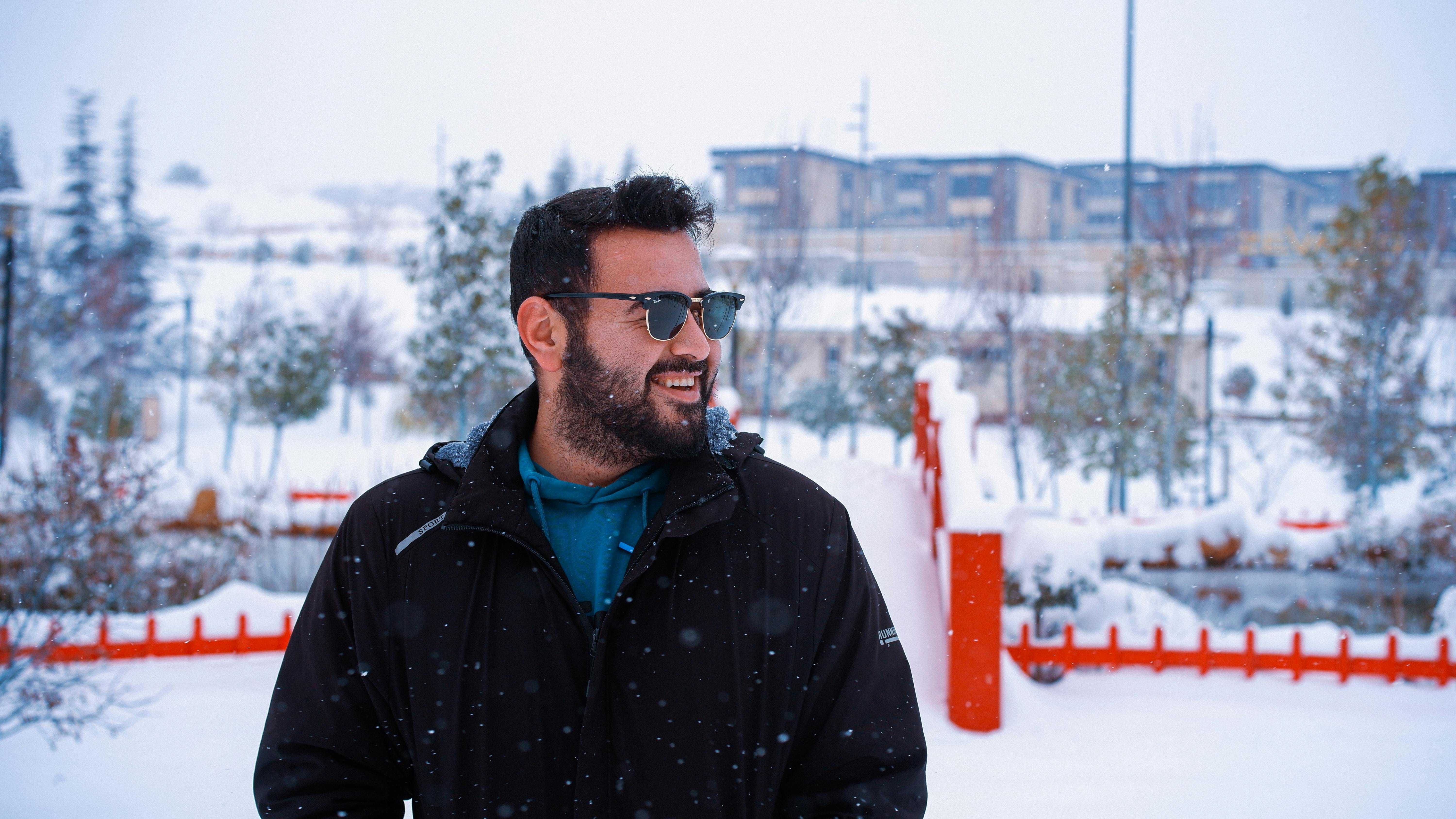 De franc Home amb ulleres de sol somrient en un entorn exterior nevat, ambient hivernal. Foto d'estoc