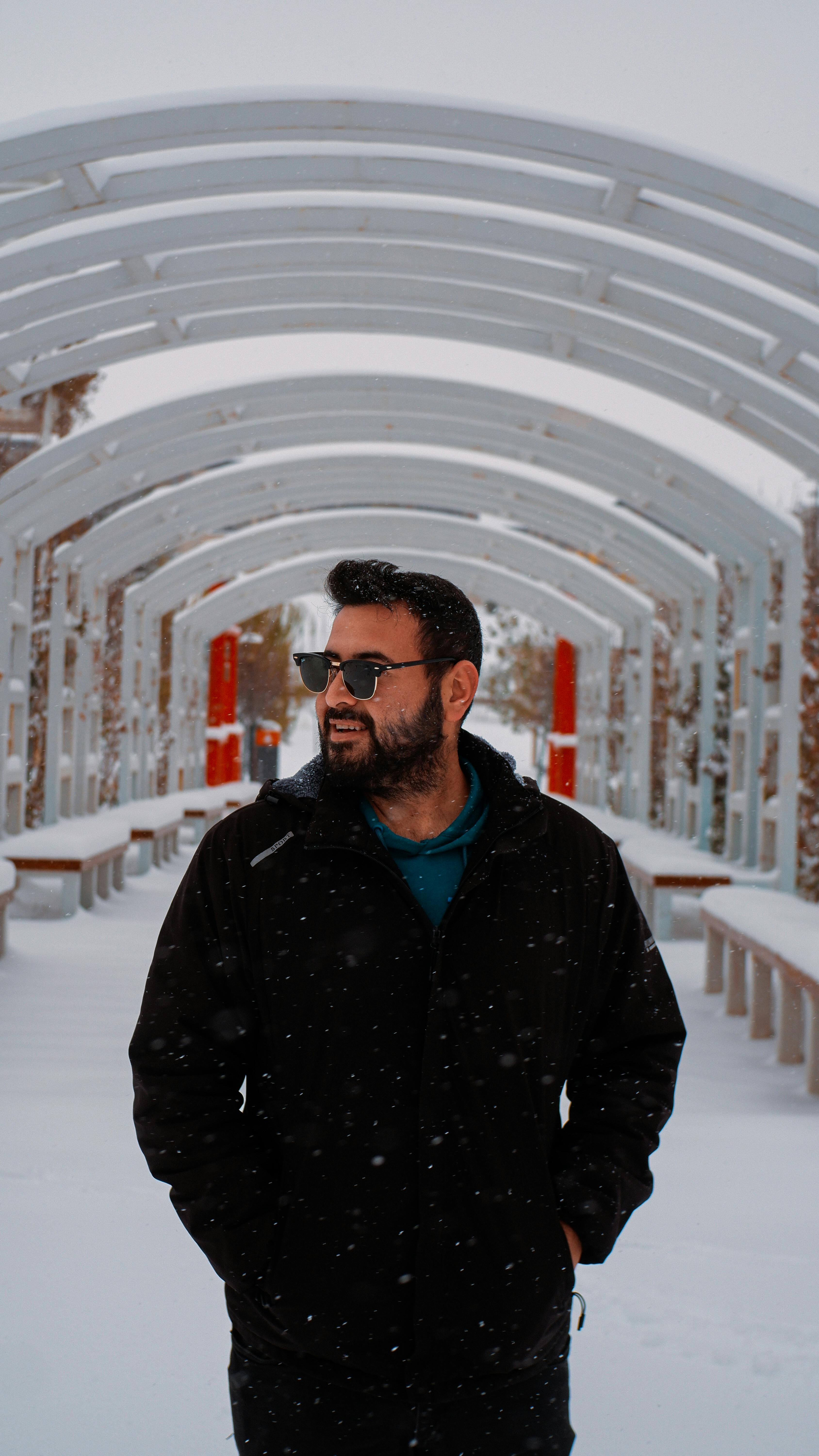 De franc Home amb un abric negre caminant per un camí cobert de neu amb arcs blancs. Foto d'estoc