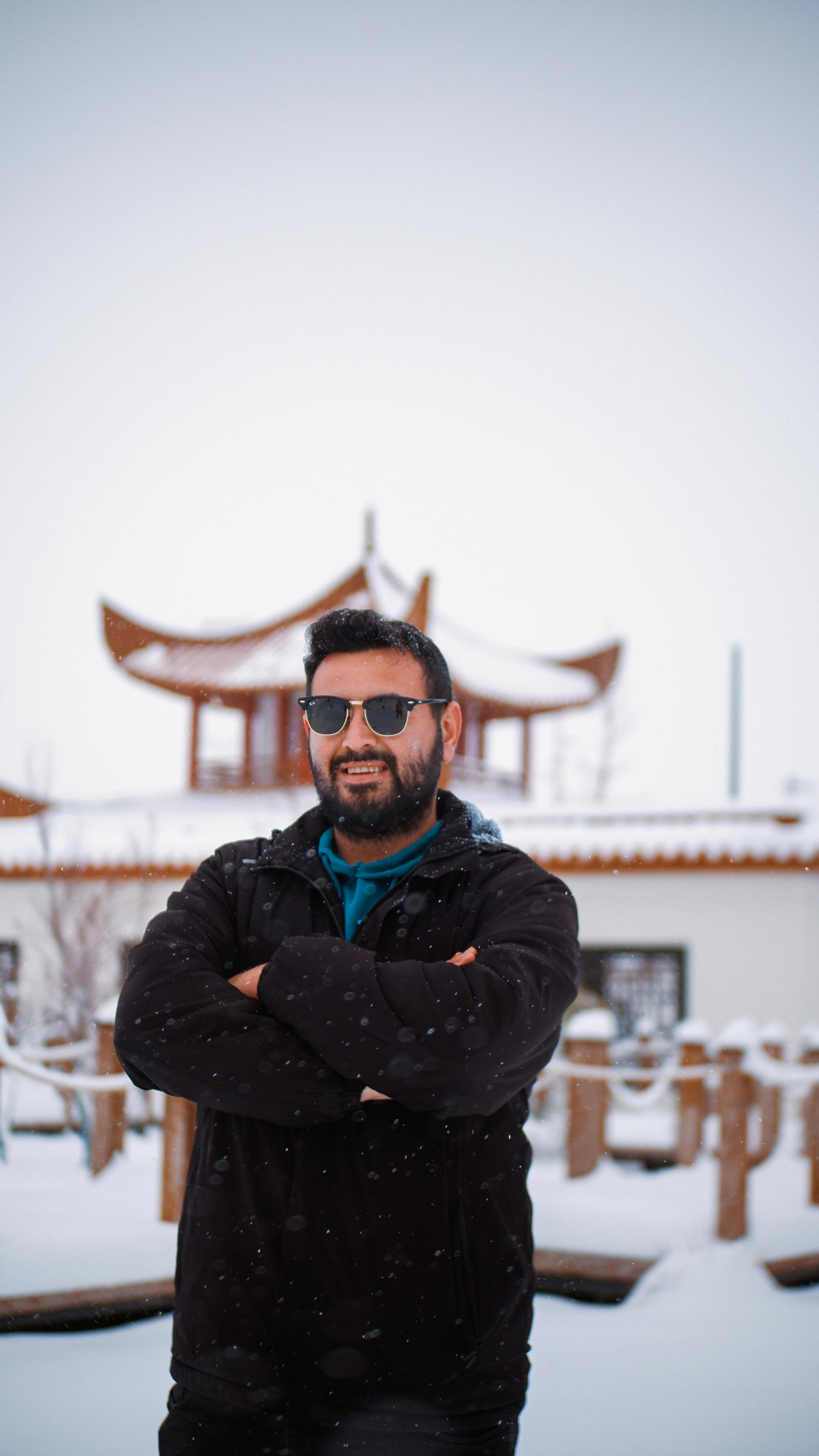 De franc Un home amb ulleres de sol i abric d'hivern es troba a la neu amb una pagoda tradicional al darrere. Foto d'estoc