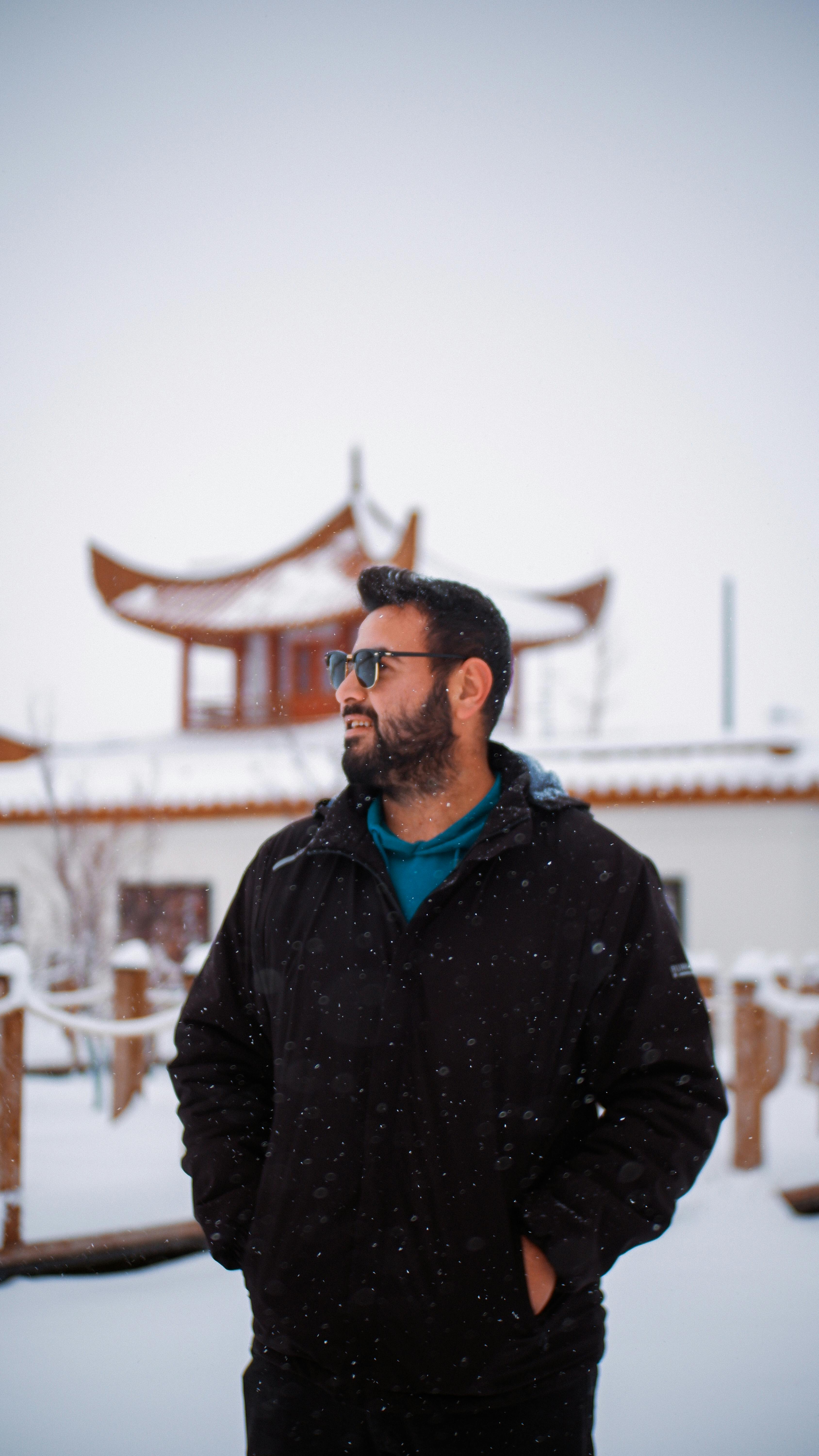 De franc Un home amb abric negre es troba a la neu amb arquitectura asiàtica al fons. Foto d'estoc