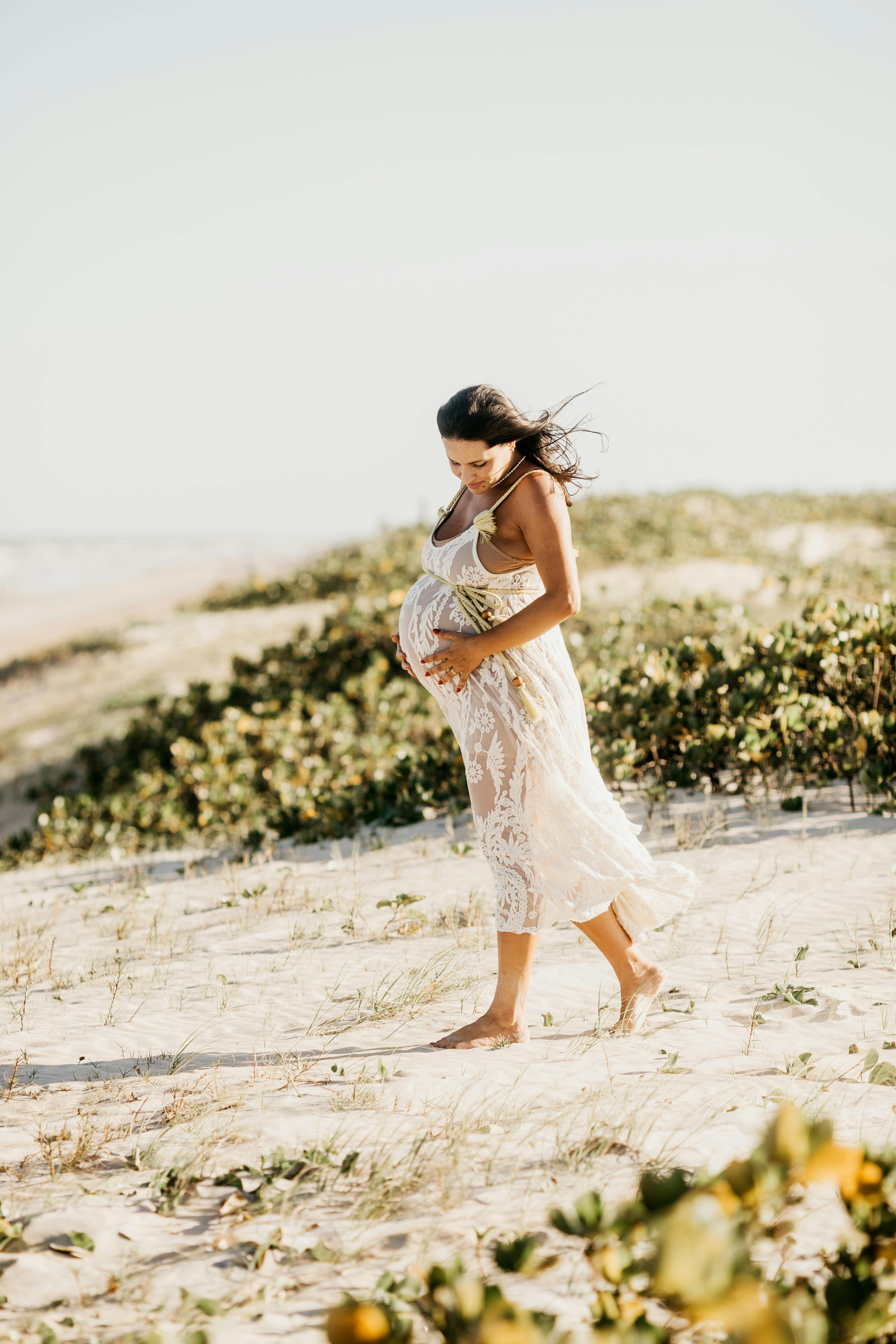 pregnant woman in white dress walking on beach