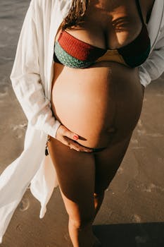 阳光明媚的海滩上，一名穿着比基尼的孕妇捂着肚子