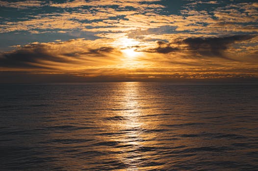 A serene sunset over a calm ocean with golden tones reflecting on the water.