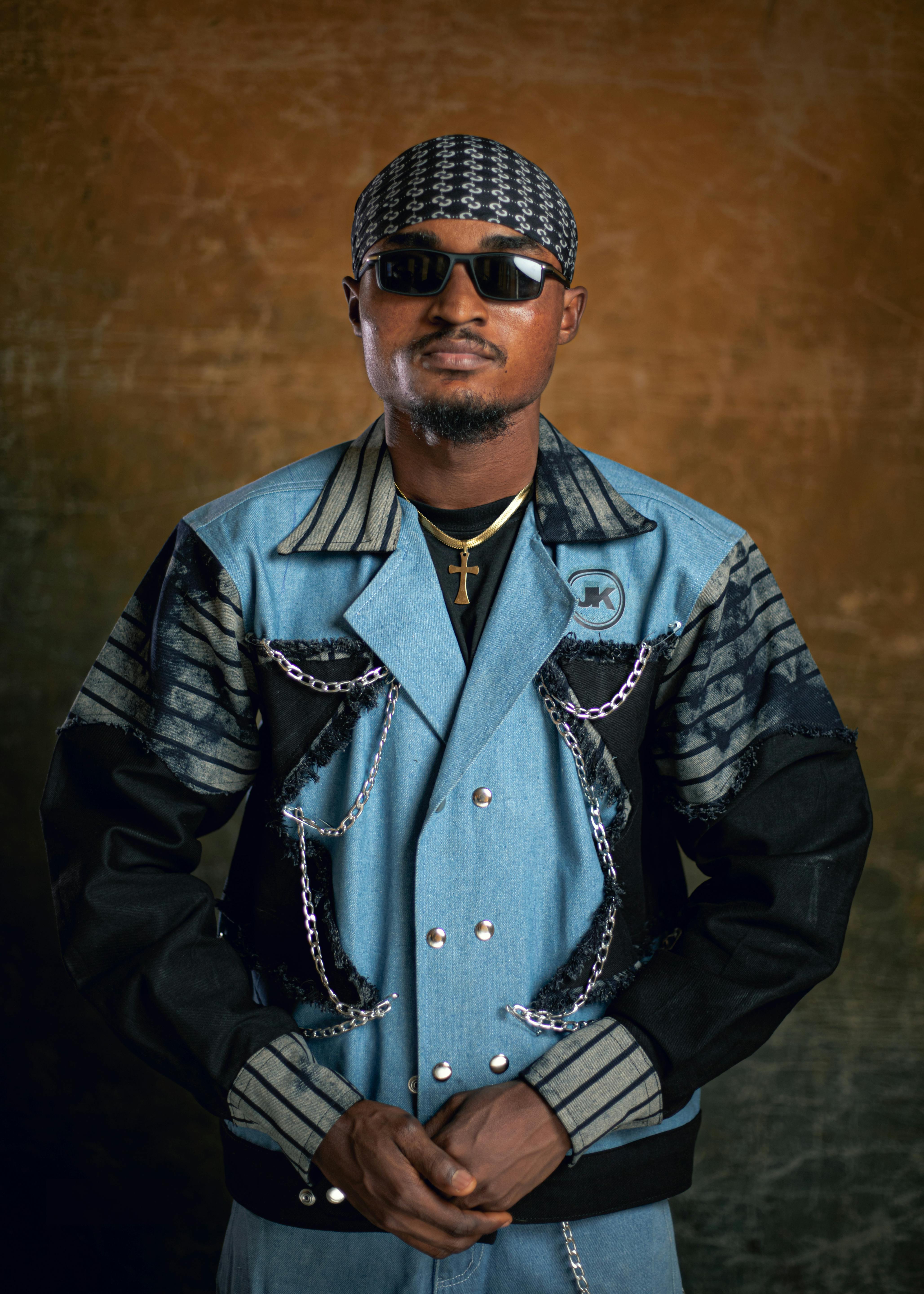 Fashionable man wearing a denim jacket with chains, sunglasses, and a beanie, exuding confidence.