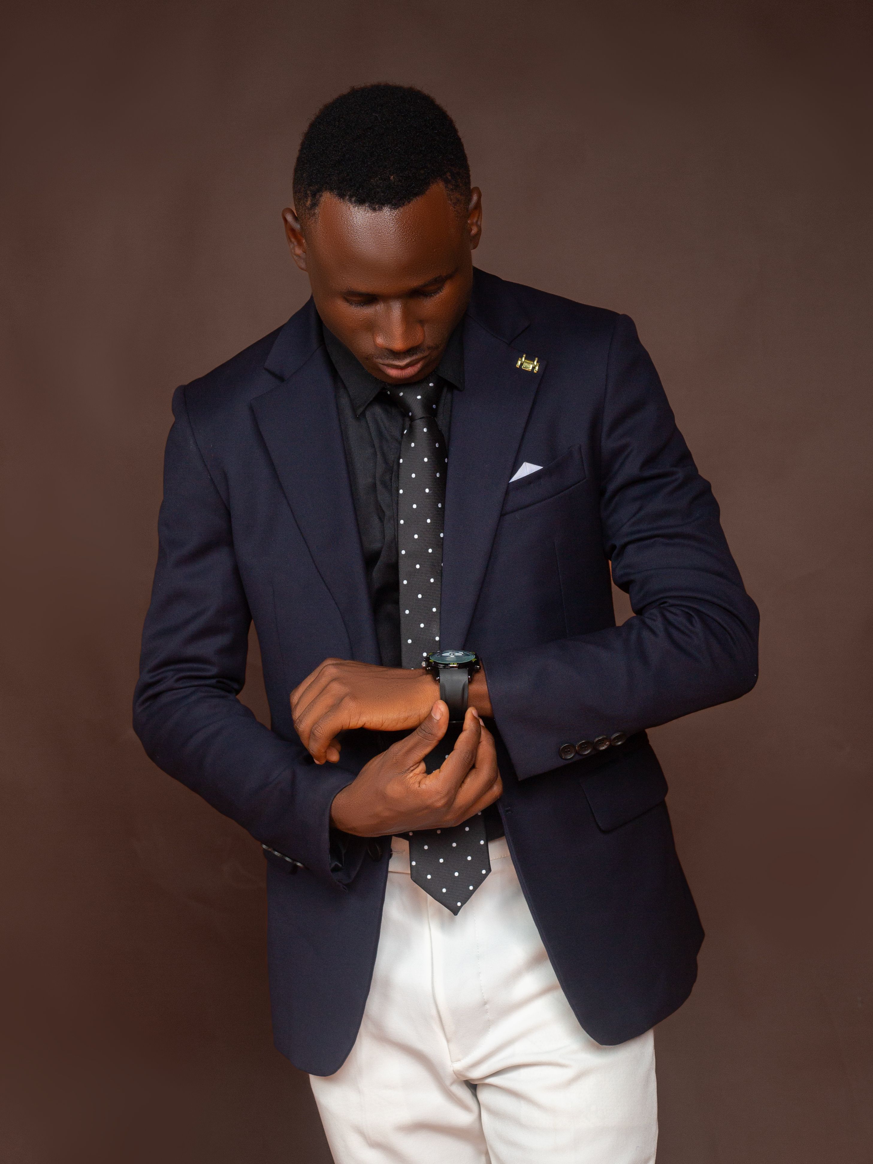 Elegant black man in navy suit adjusting watch, exuding professionalism.