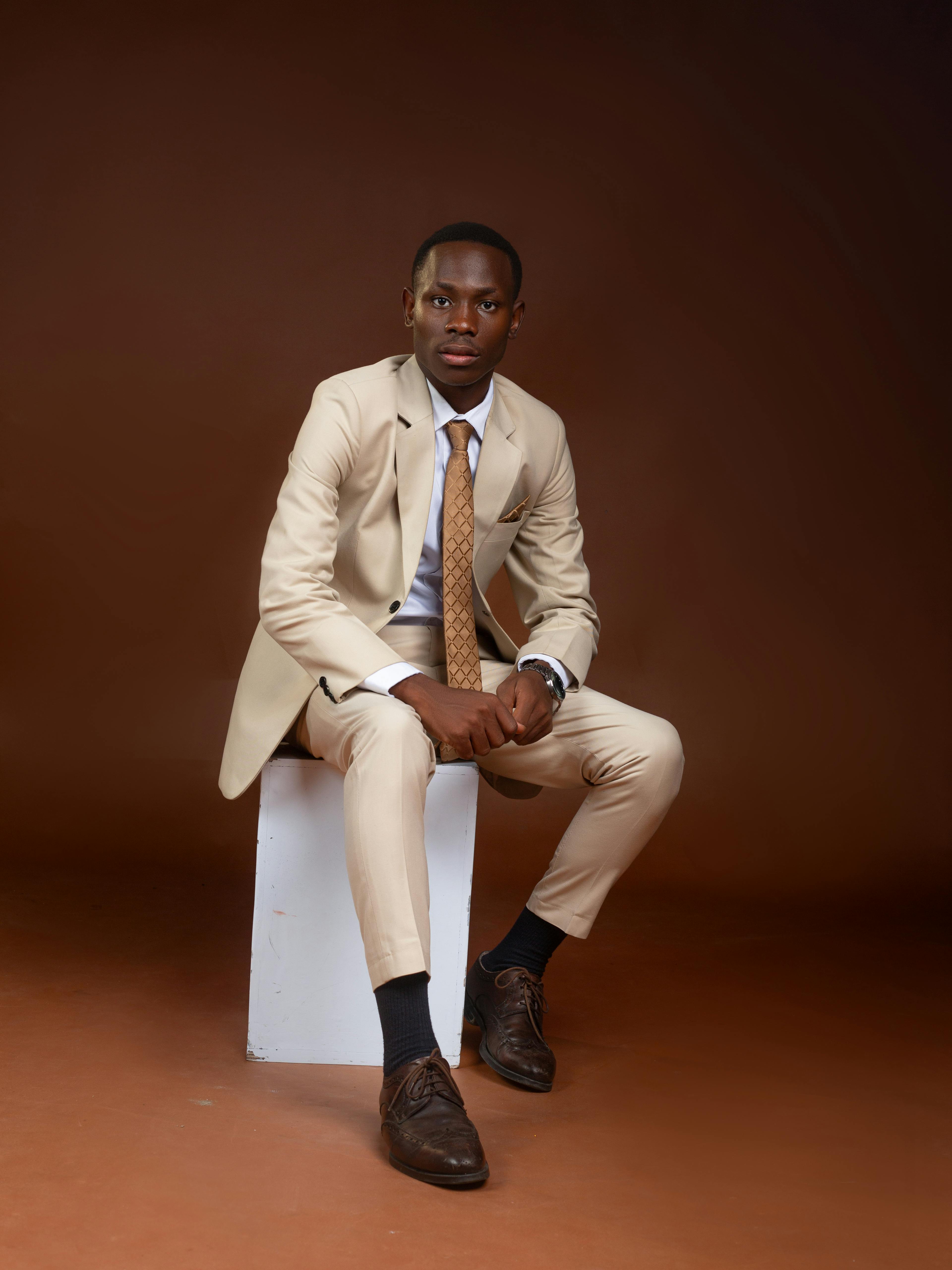 Gratis Hombre elegante con traje beige sentado sobre un fondo marrón. Retrato profesional. Foto de stock