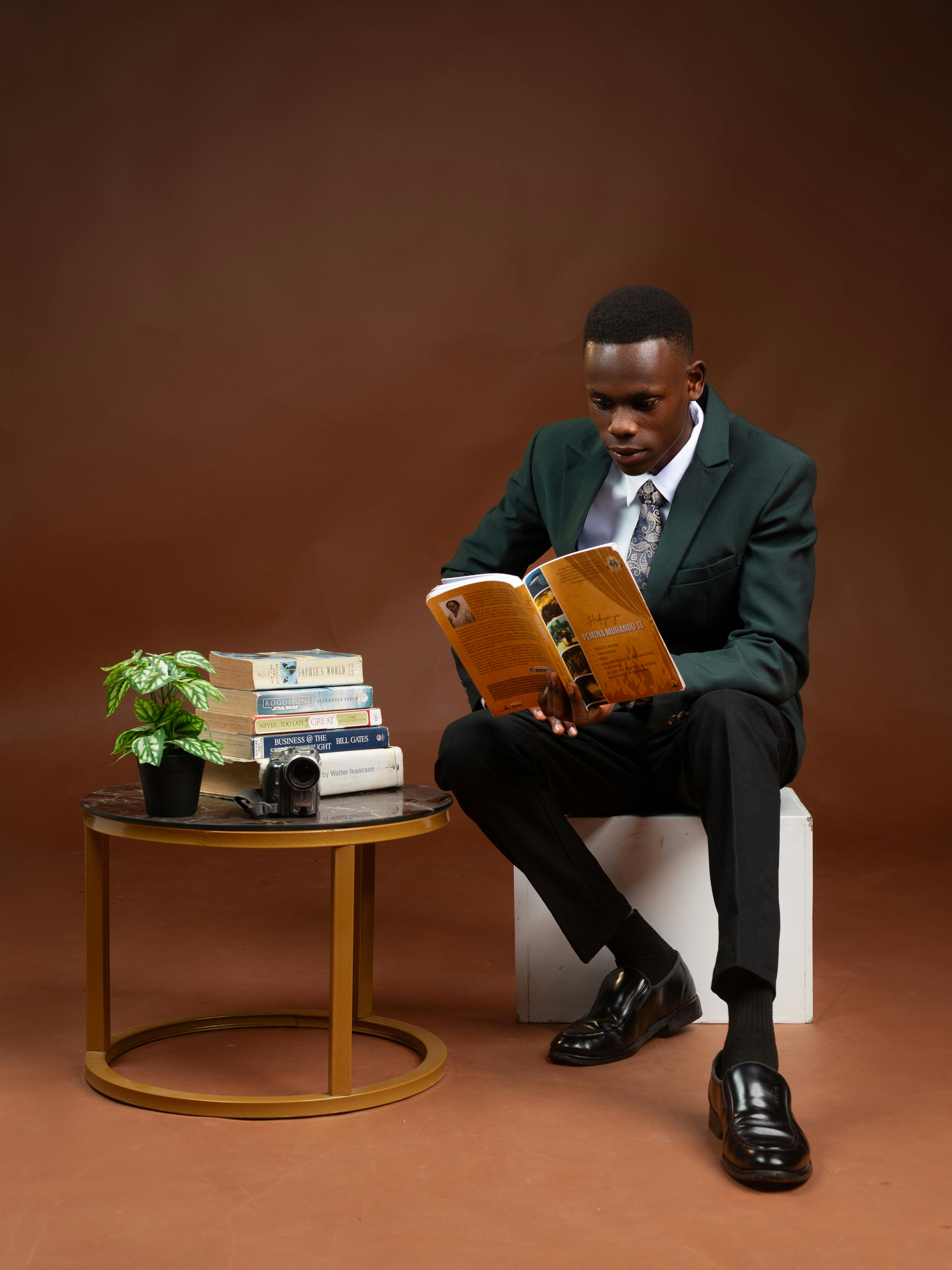 Gratis Adulto joven con traje leyendo un libro en el interior con una configuración minimalista ordenada, que promueve la concentración y la relajación. Foto de stock