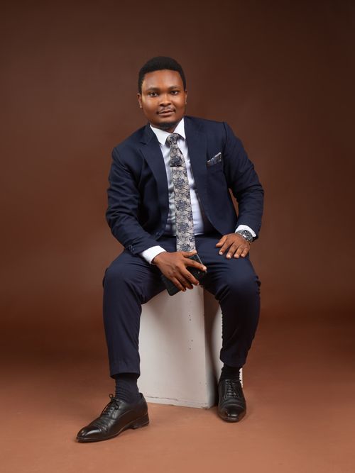 Free Portrait of a confident man in a navy suit, sitting against a brown studio backdrop. Stock Photo