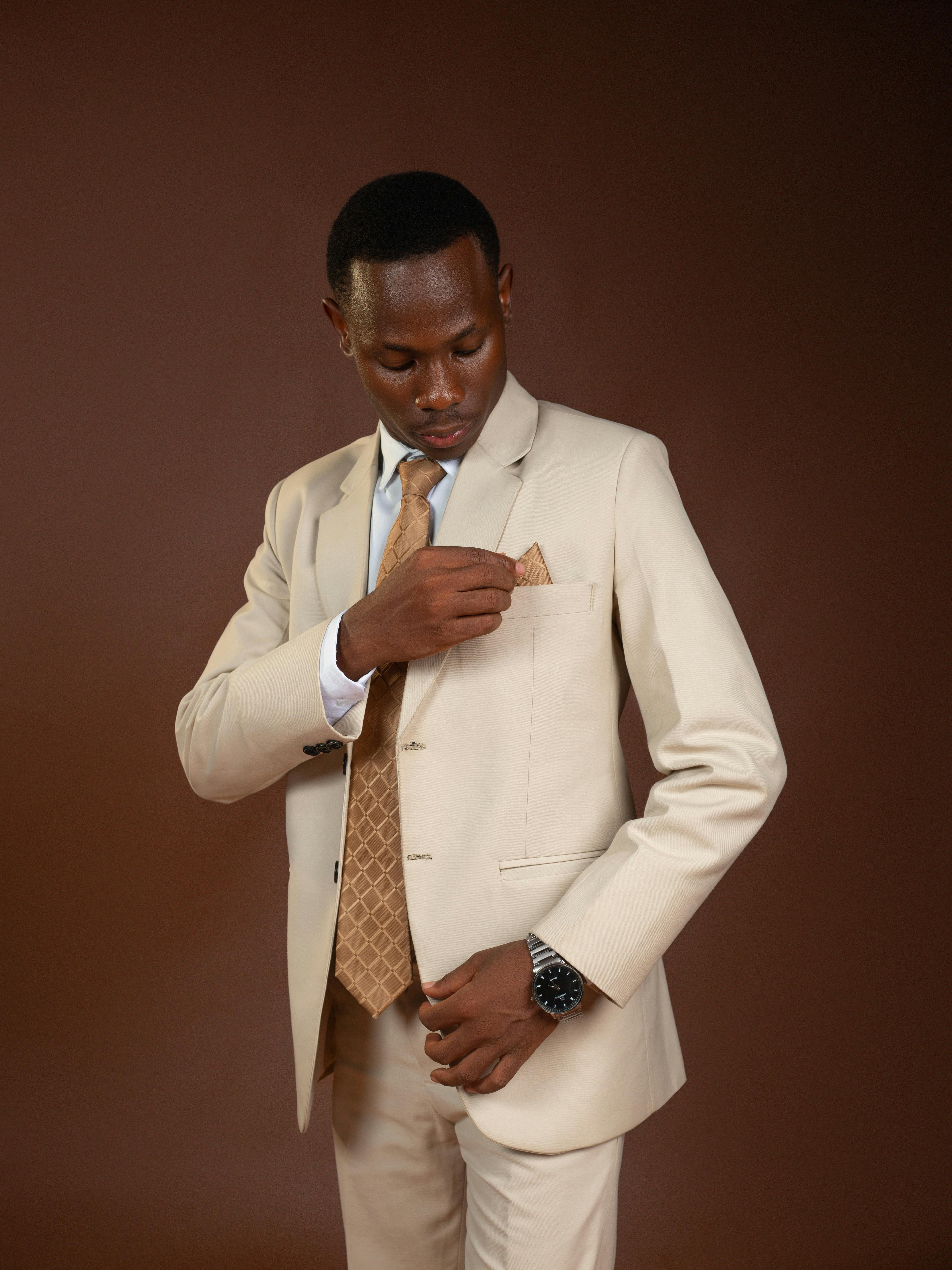 Gratis Hombre profesional con traje beige ajustando un pañuelo de bolsillo sobre un fondo marrón. Foto de stock