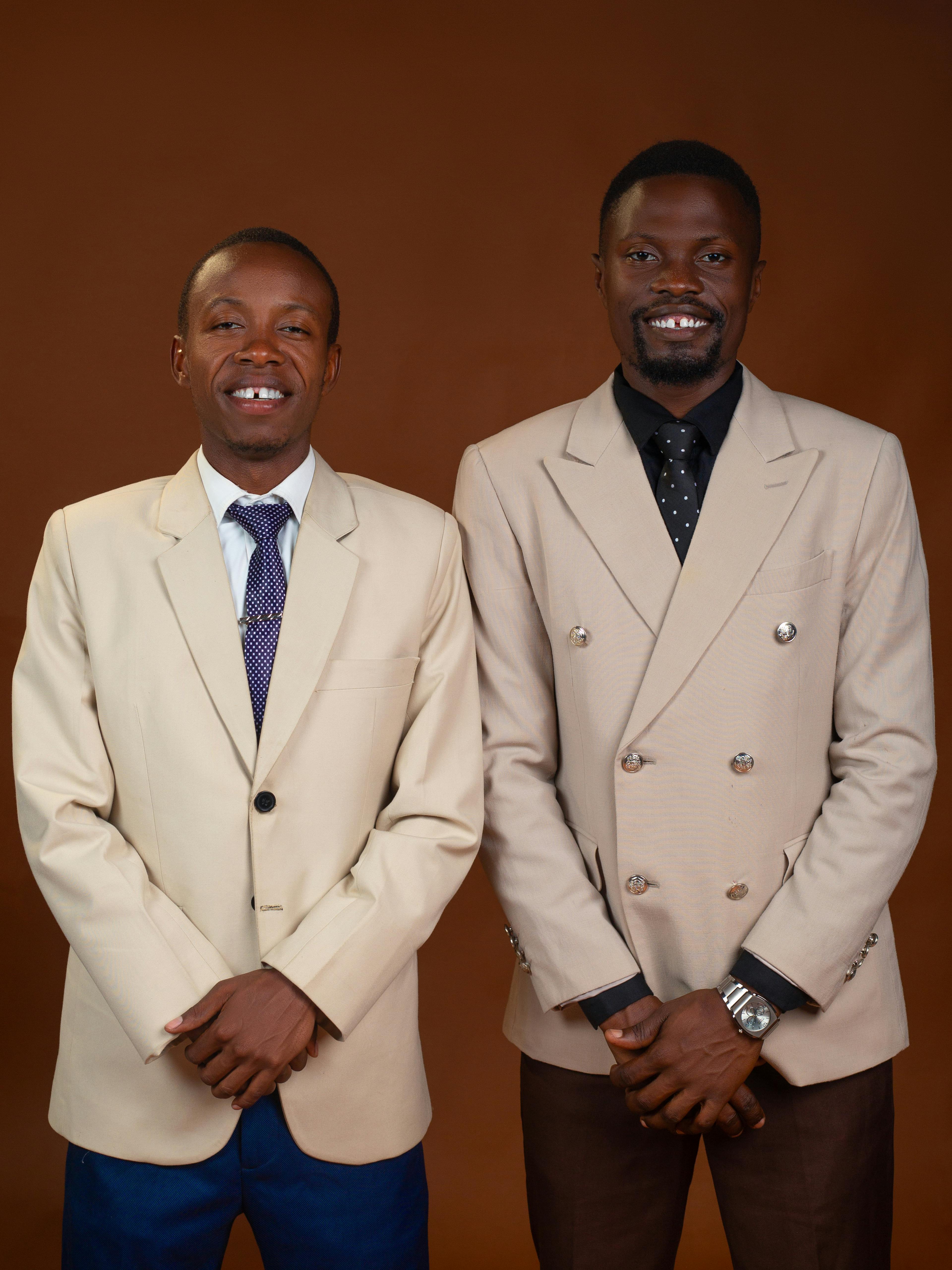 Gratis Dos hombres sonrientes, vestidos con trajes beige, en un estudio sobre un fondo marrón. Foto de stock