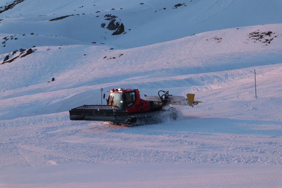A snow grooming machine prepares a ski slope during a picturesque sunset in winter mountains.