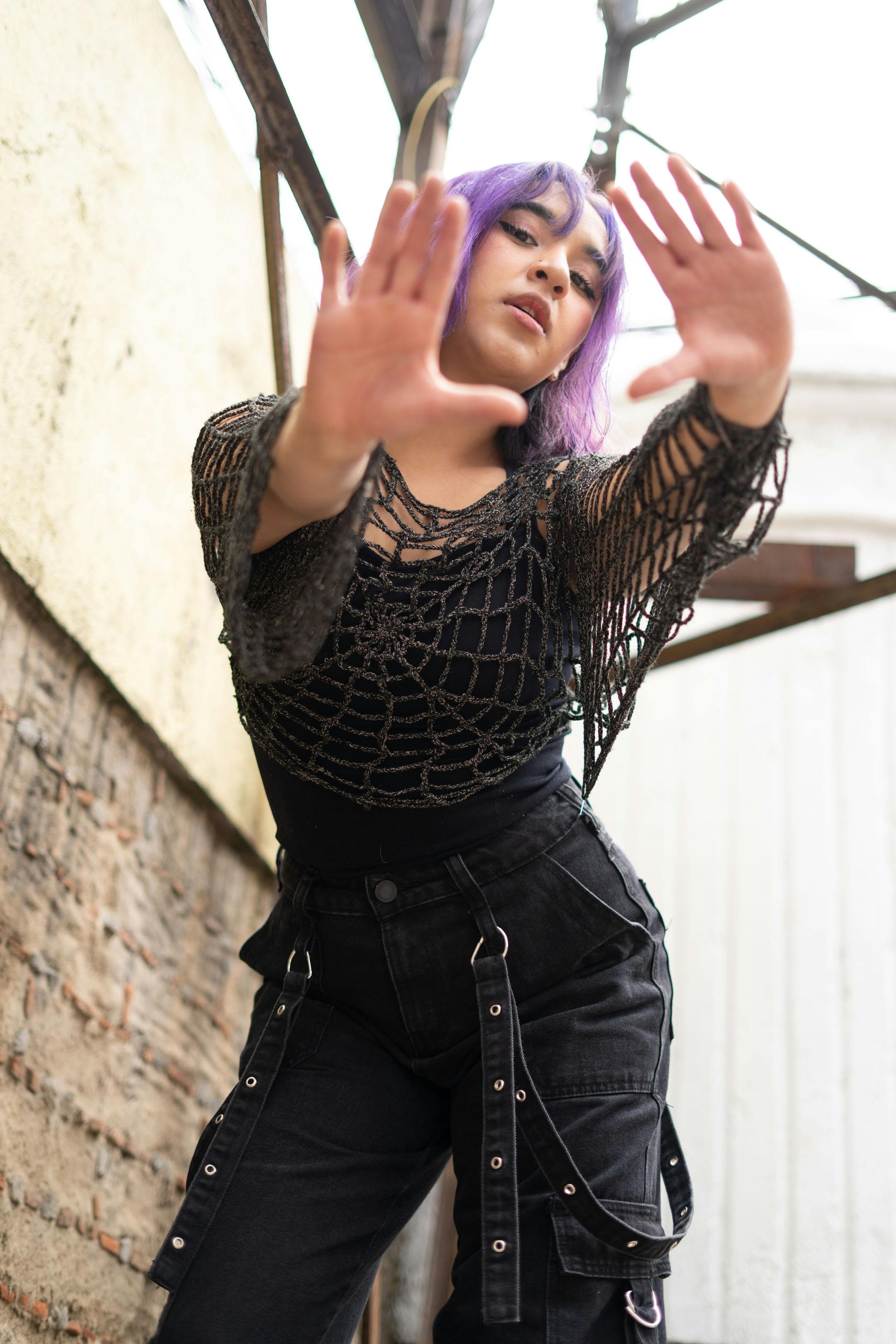 grátis Mulher jovem e estilosa, com cabelo roxo e suéter com estampa de teia, posando em um ambiente urbano. Foto profissional