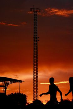 Two people silhouette against a fiery sunset with a tall structure nearby.