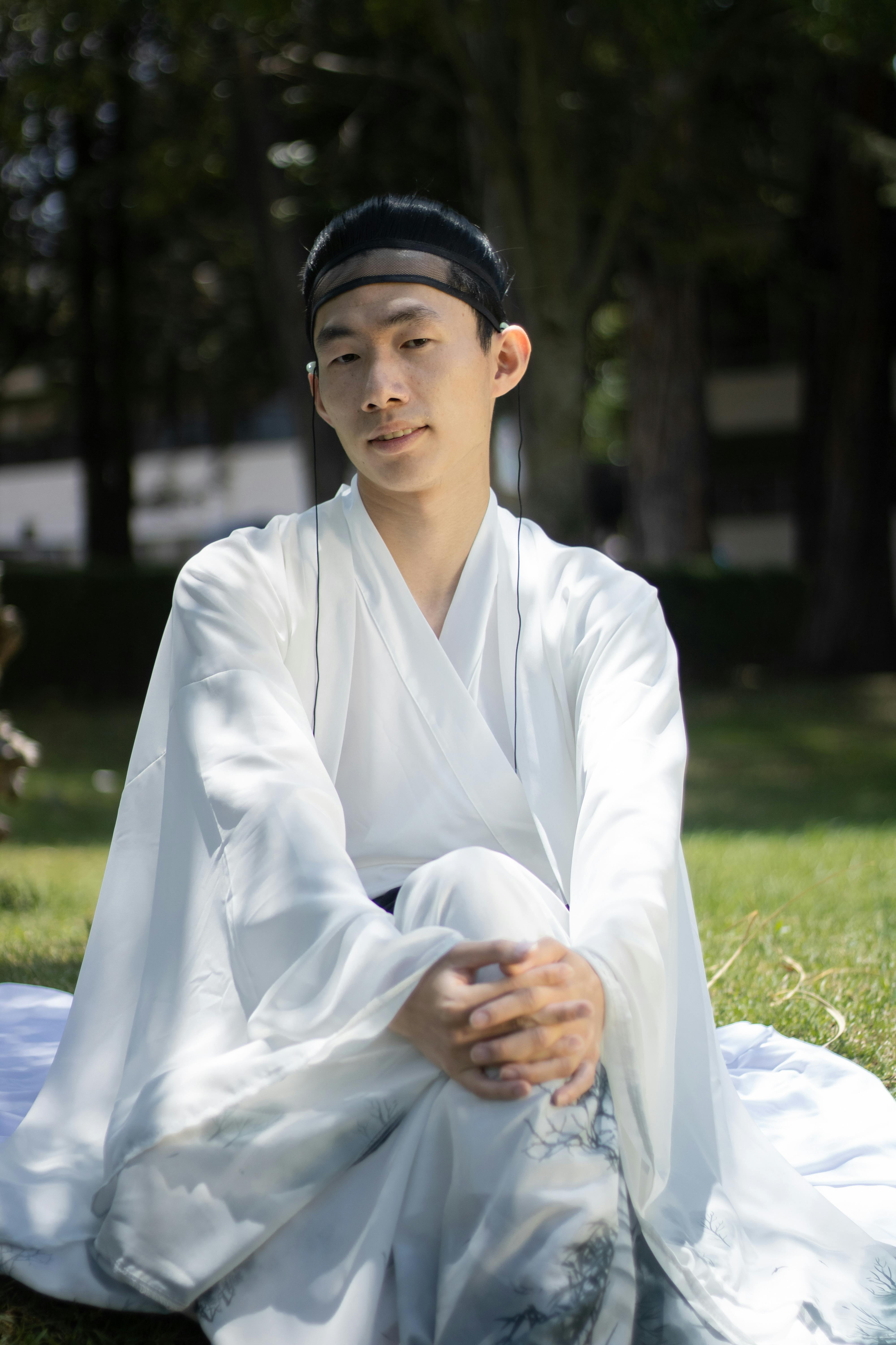 Young man wearing traditional white clothing sits peacefully in a sunny garden.