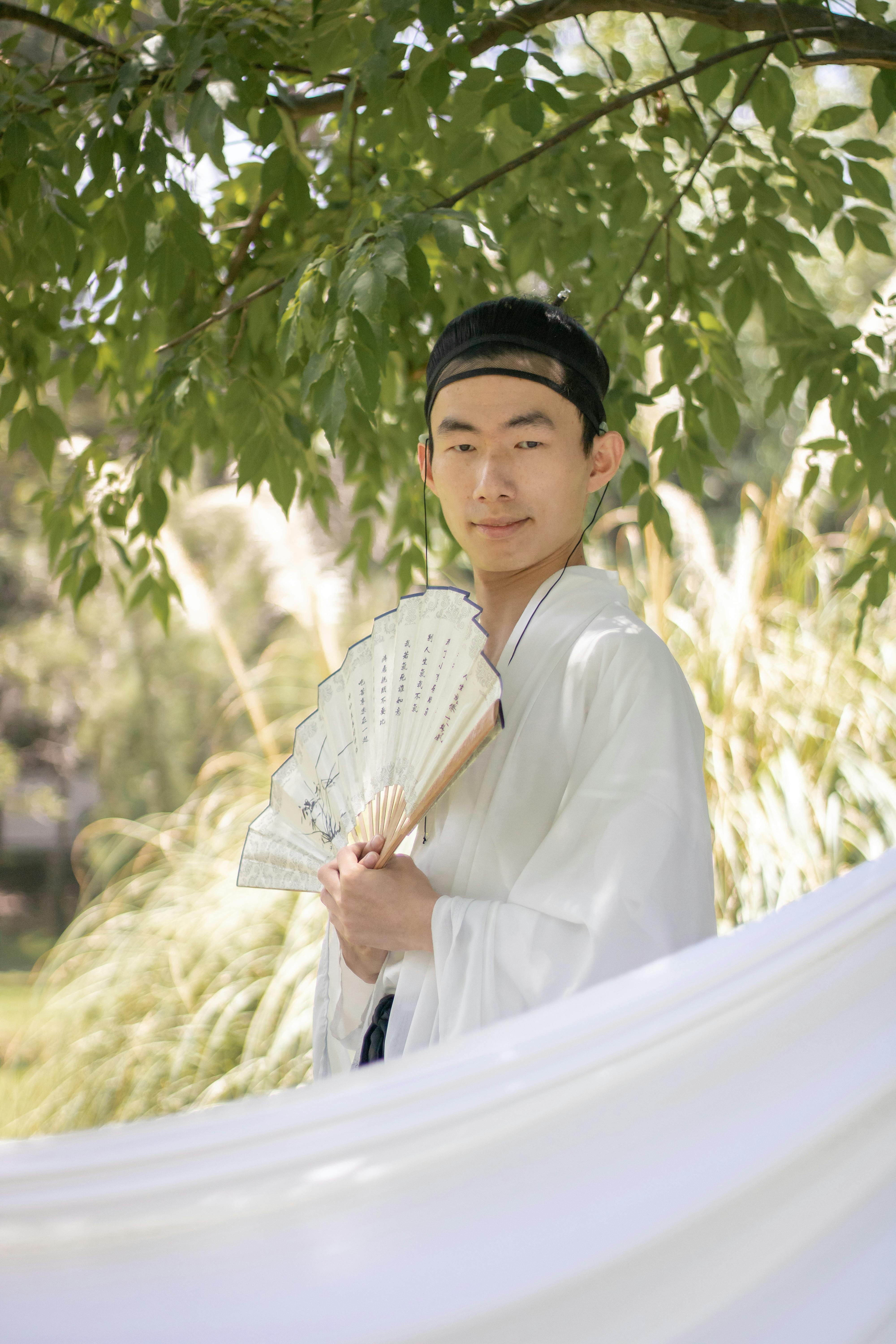 grátis Retrato de um jovem em trajes tradicionais segurando um leque ao ar livre. Foto profissional