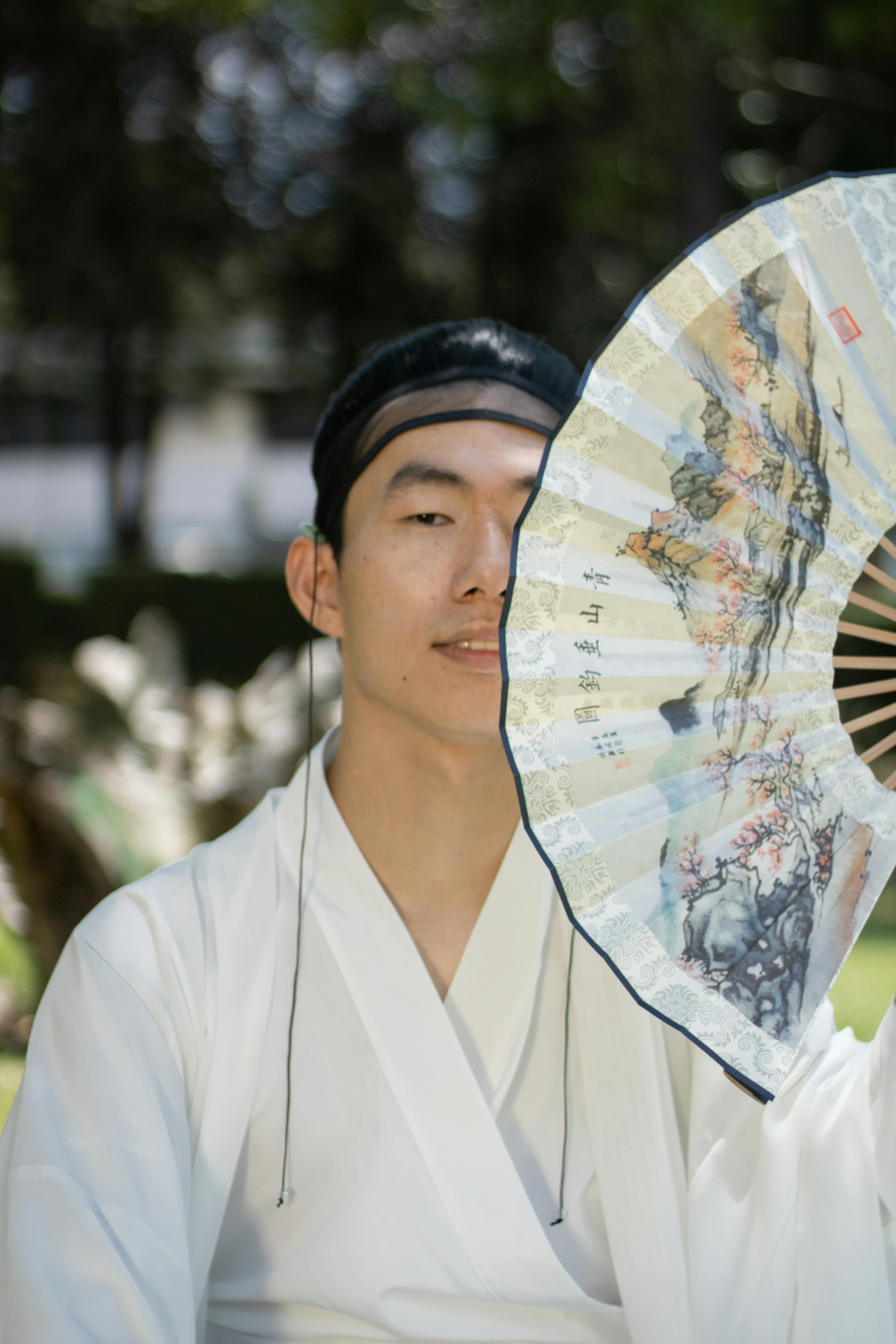 grátis Homem em trajes tradicionais do Leste Asiático segurando um leque ornamentado ao ar livre. Foto profissional
