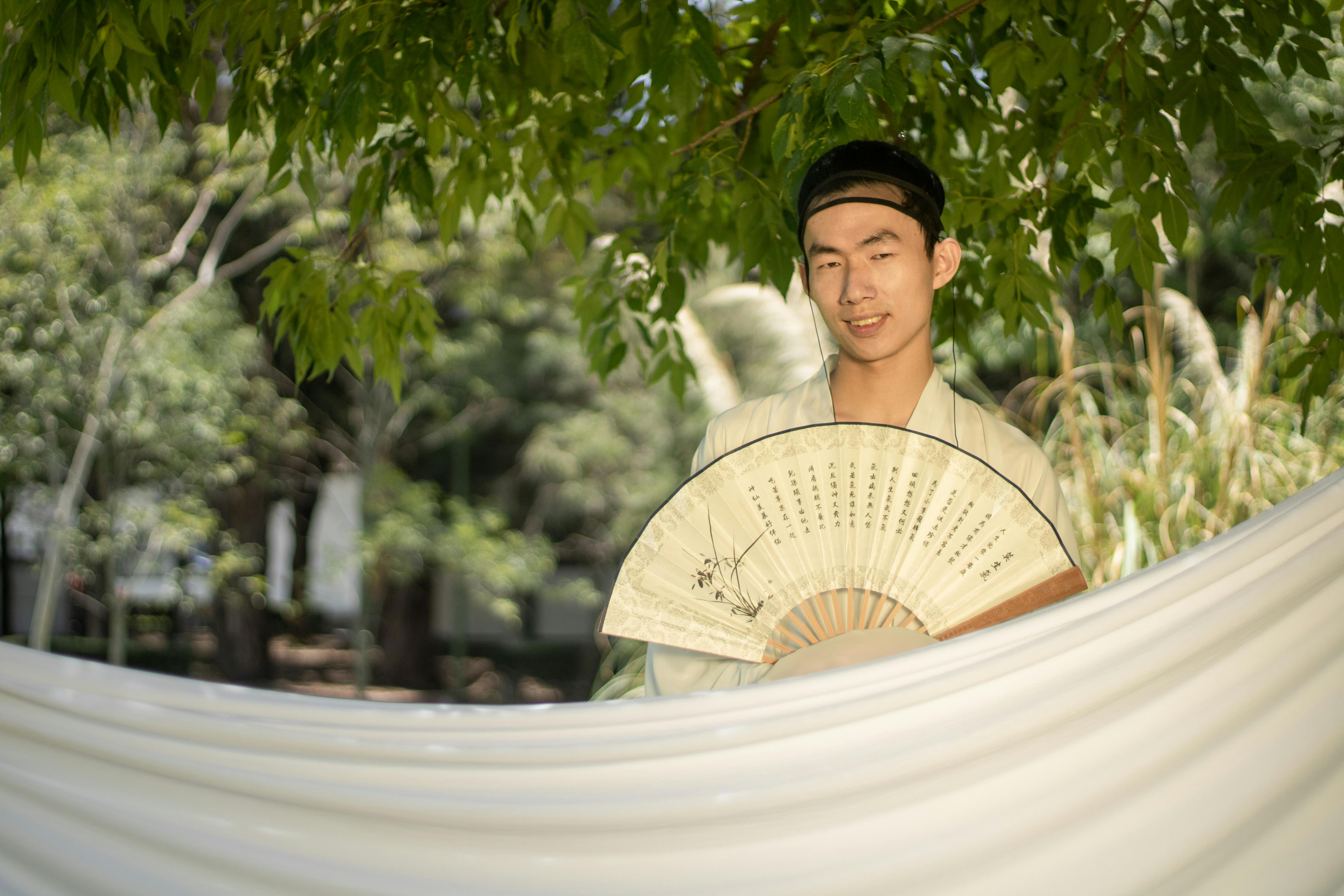 grátis Jovem segurando um leque tradicional ao ar livre em meio à vegetação. Foto profissional