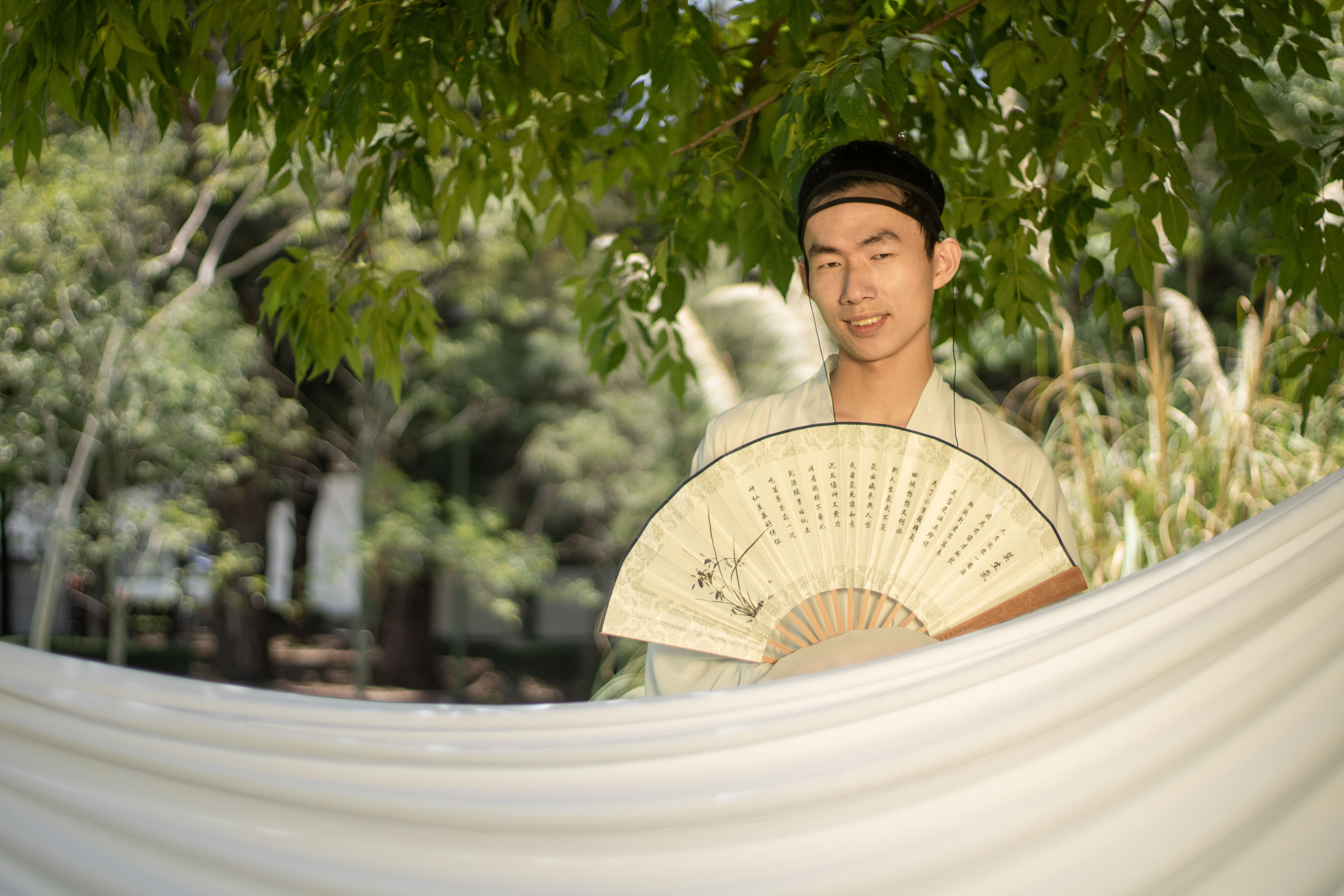 Young Man with Traditional Fan in Garden Setting · Free Stock Photo