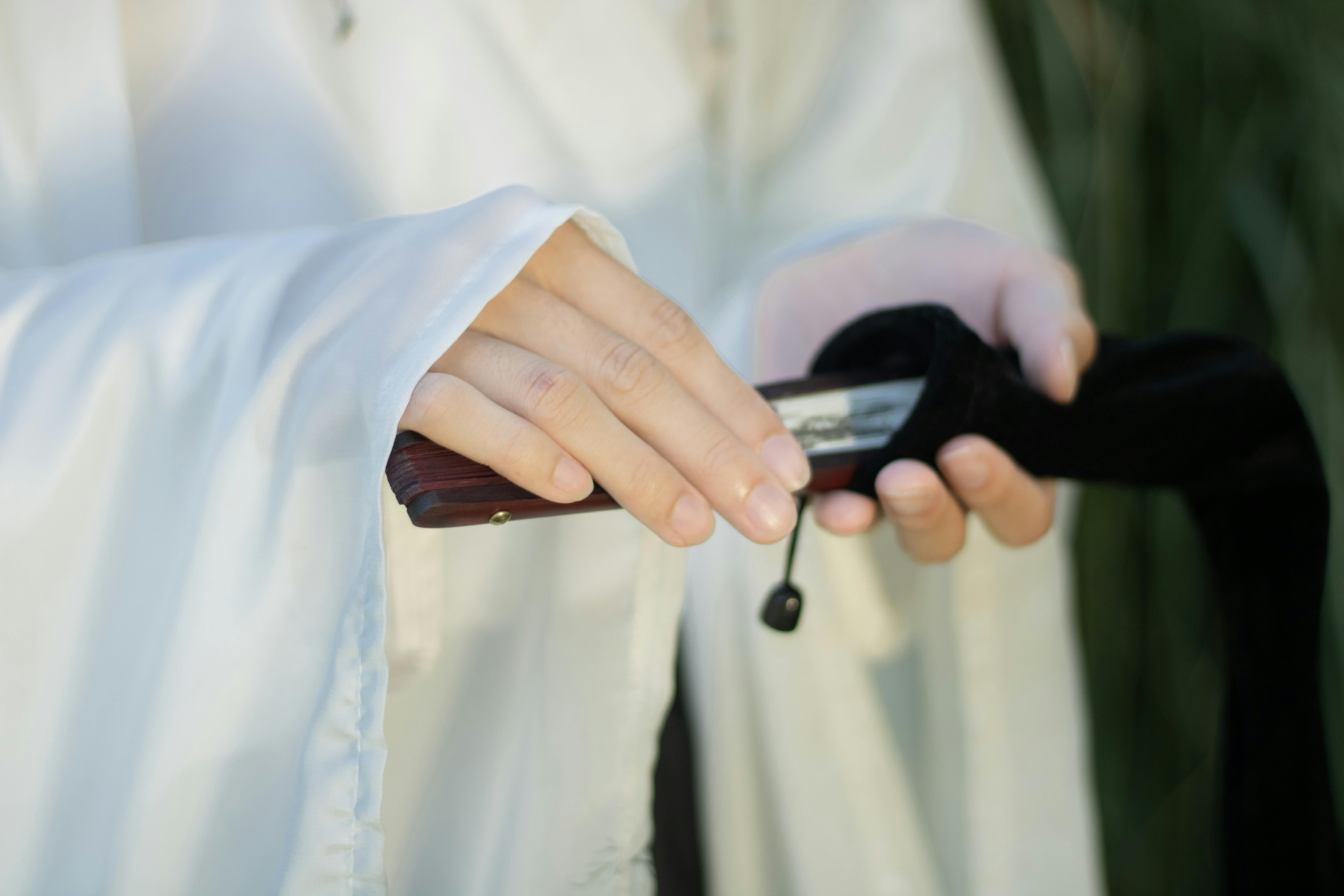 grátis Close-up de mãos vestidas com um traje tradicional segurando uma espada embainhada, enfatizando a herança cultural. Foto profissional