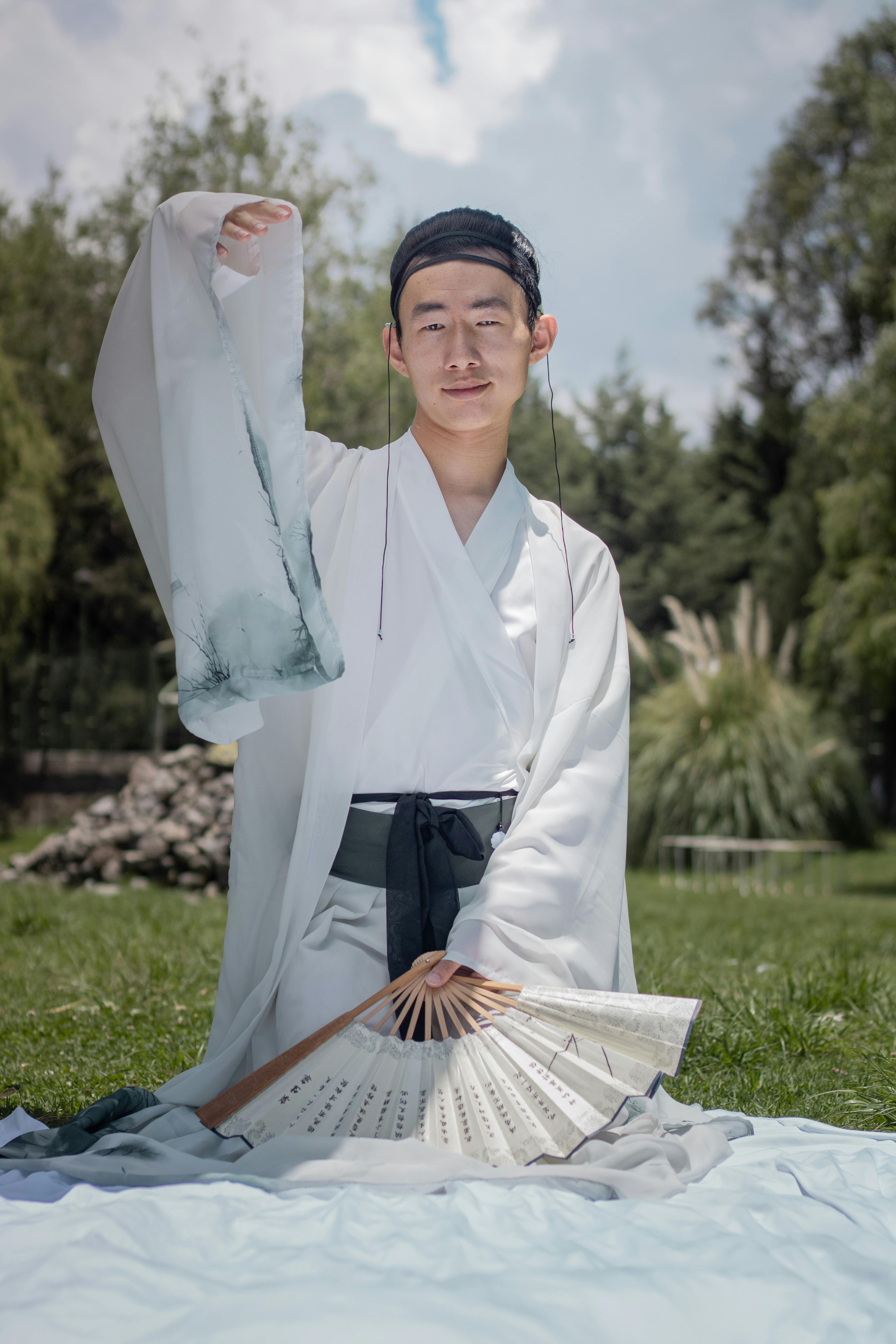 grátis Homem em traje tradicional asiático posando ao ar livre com um leque. Foto profissional