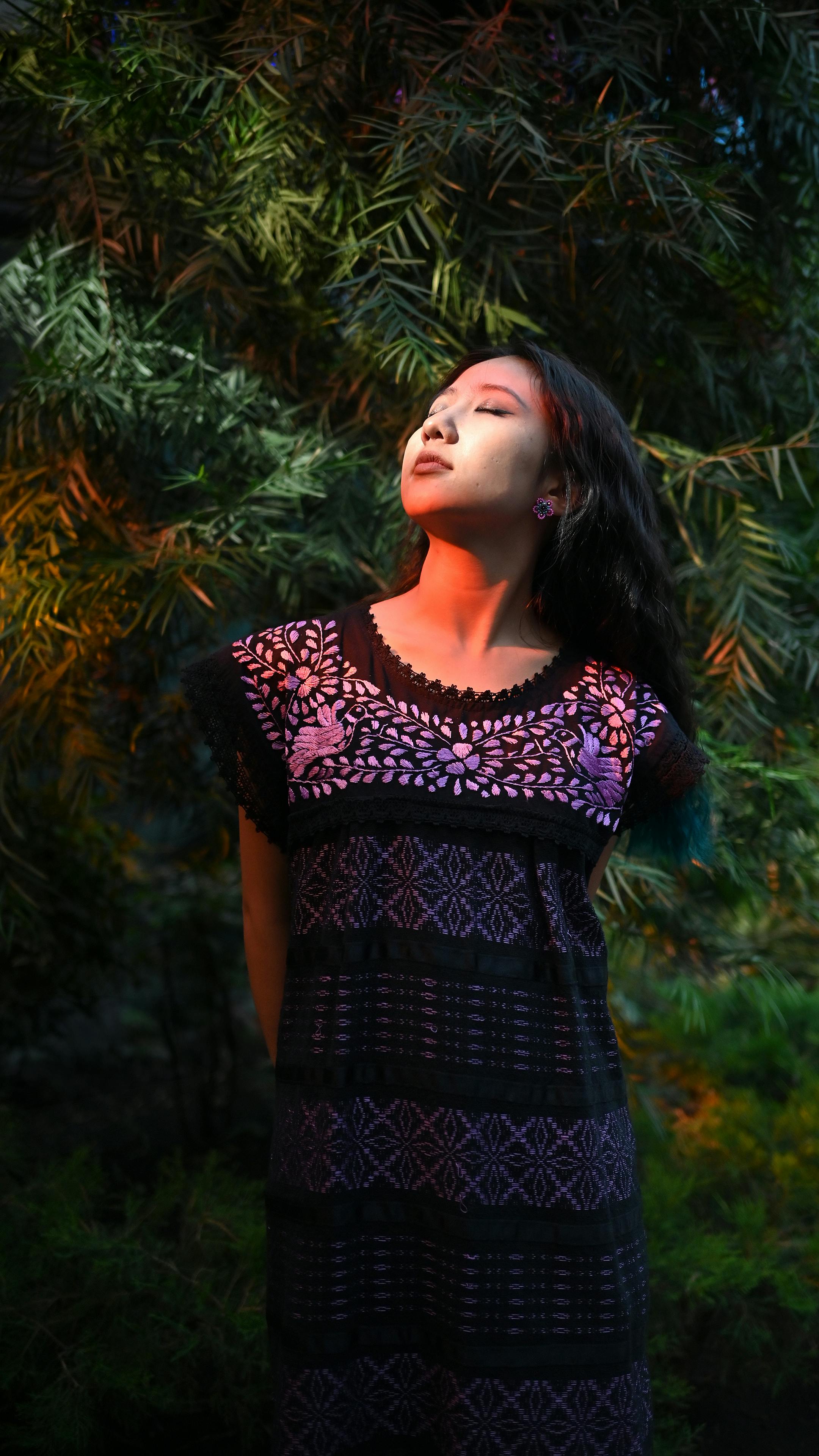 grátis Uma mulher com um vestido estampado, iluminada por cores vibrantes, está em meio a uma vegetação exuberante. Foto profissional