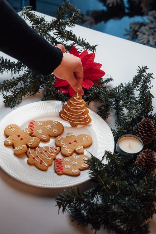 Free Hand reaching for holiday gingerbread cookies on a decorated table with fir branches and candles. Stock Photo