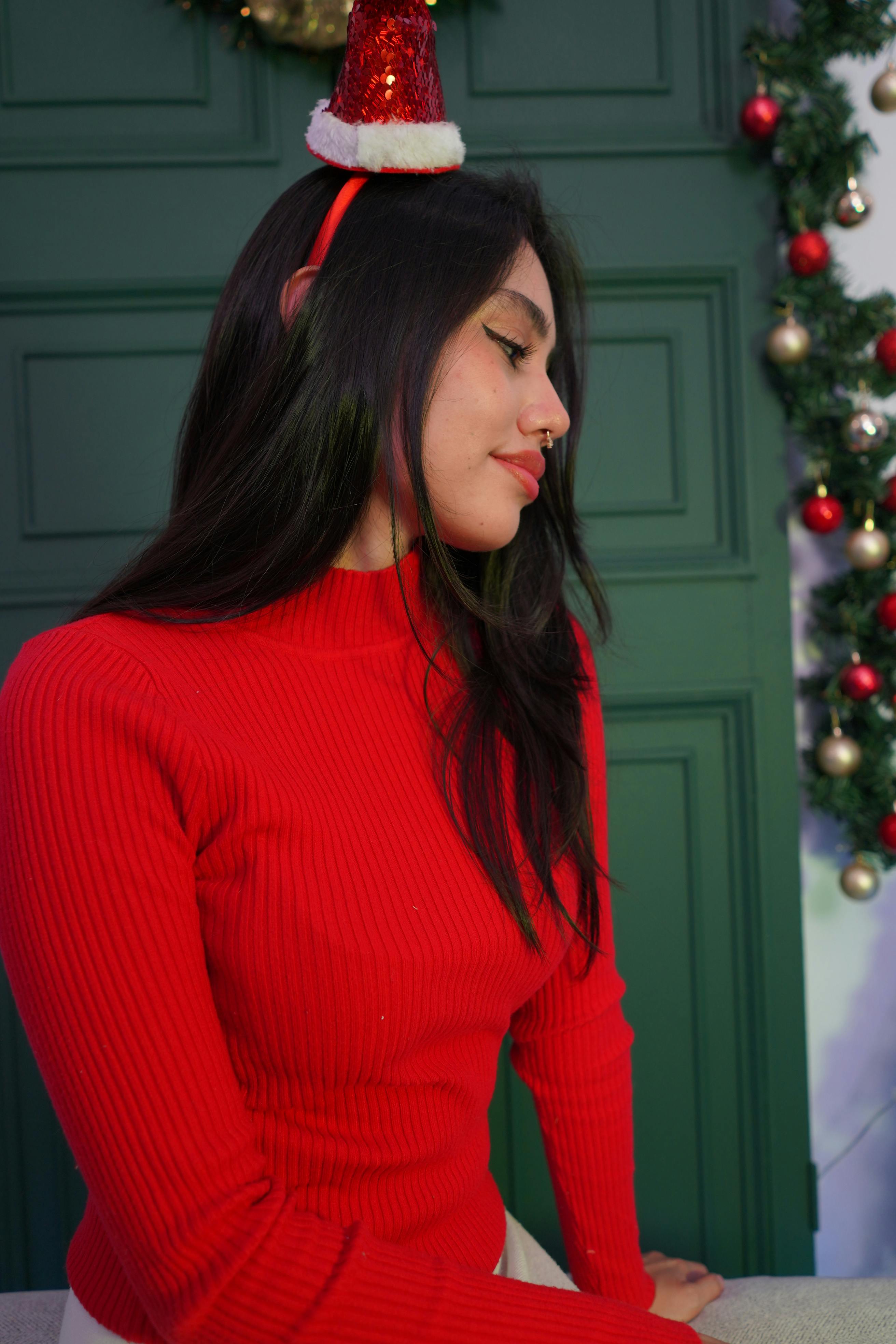 grátis Mulher com suéter vermelho e gorro de Papai Noel com enfeites natalinos. Foto profissional