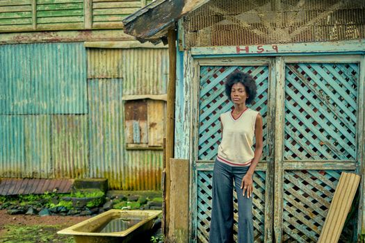 A woman standing by a weathered building with blue lattice doors, showcasing rustic charm.