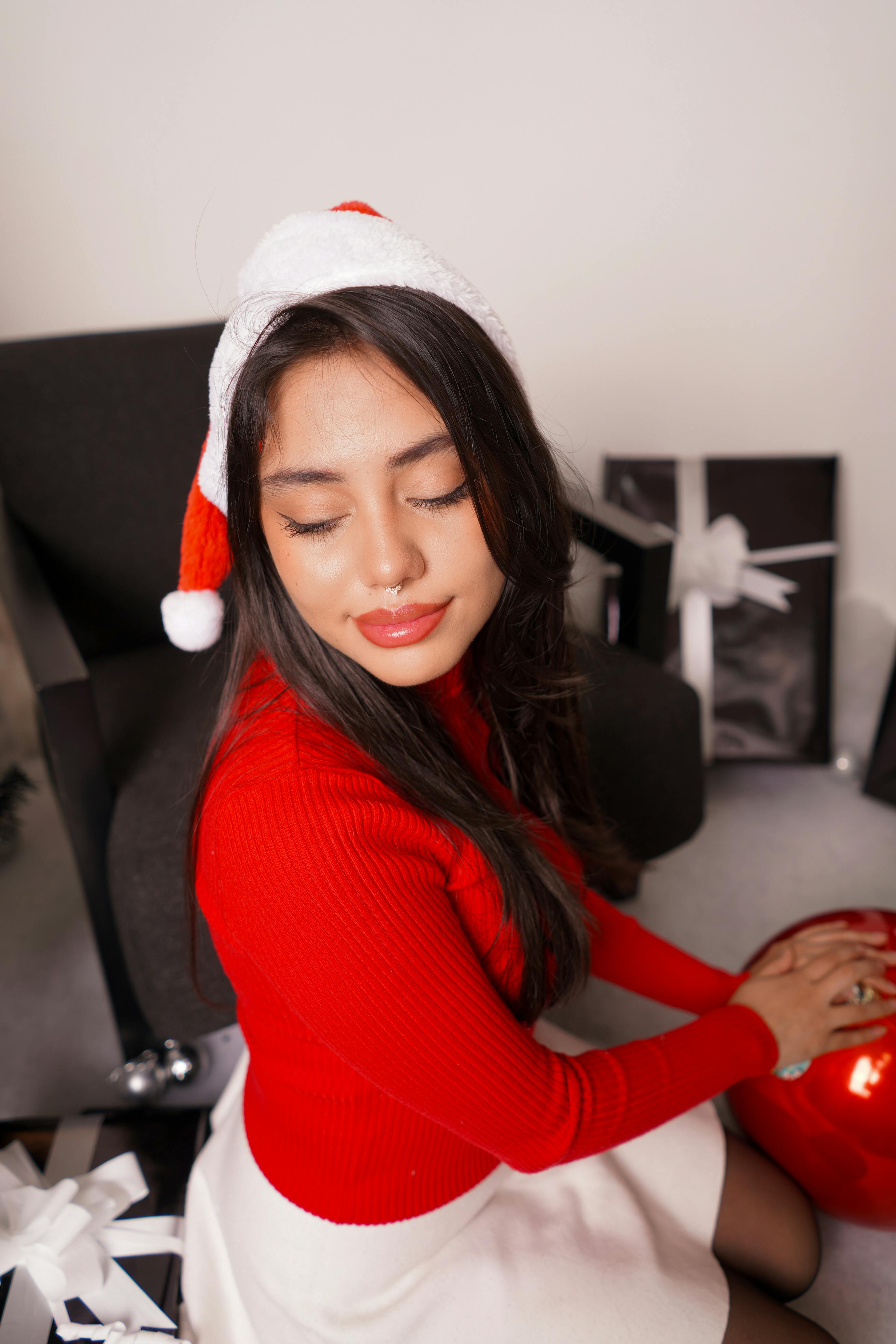 grátis Mulher com gorro de Papai Noel aproveitando um ambiente natalino aconchegante com presentes. Foto profissional