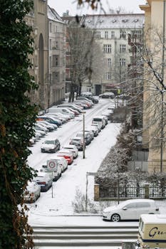 Snow blankets a quiet urban street in Berlin, showcasing parked cars and classic architecture.