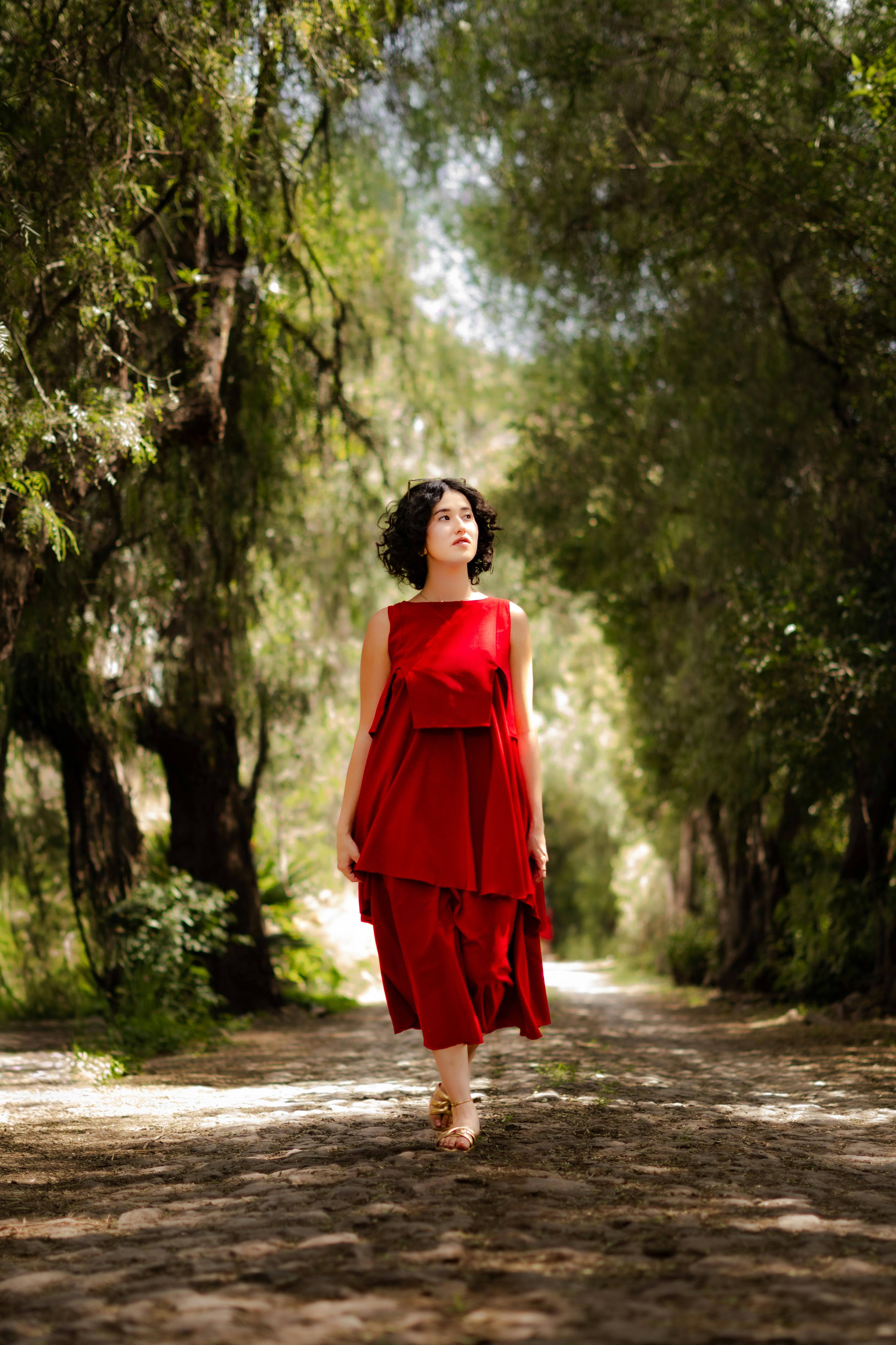 De franc Dona elegant amb vestit vermell caminant per un camí forestal assolellat a Santiago de Querétaro, Mèxic. Foto d'estoc