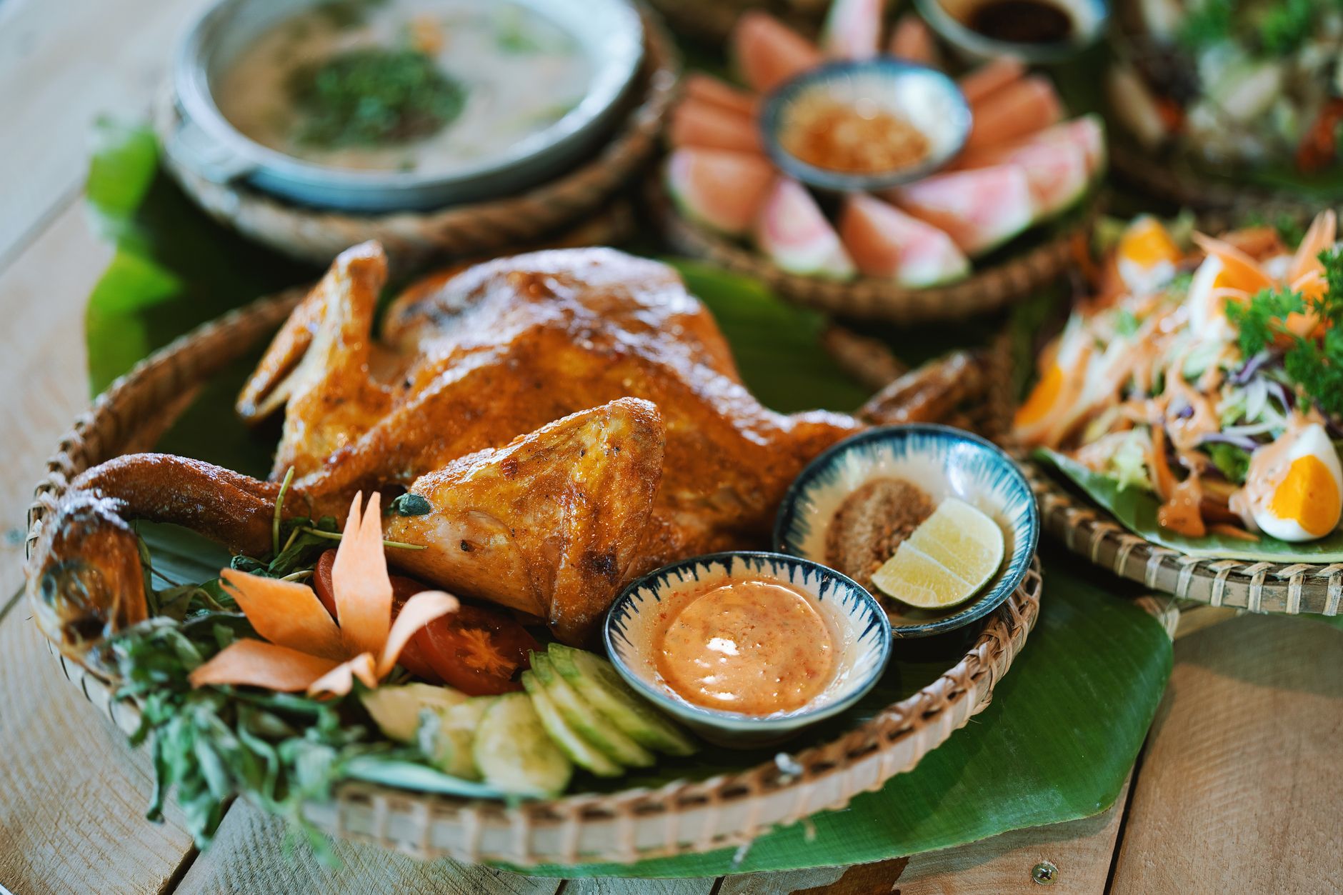 Delicious roast chicken with sauces, vegetables, and salads artfully arranged on a wooden table.