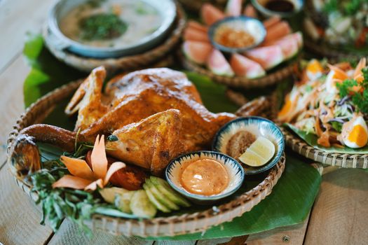 Delicious roast chicken with sauces, vegetables, and salads artfully arranged on a wooden table.
