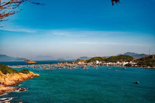 Aerial view of a picturesque coastal fishing village with boats and clear blue waters under a vibrant sky.