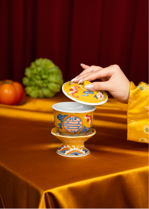 Free A hand lifts the lid of a decorative Chinese tea cup on a golden cloth. Stock Photo
