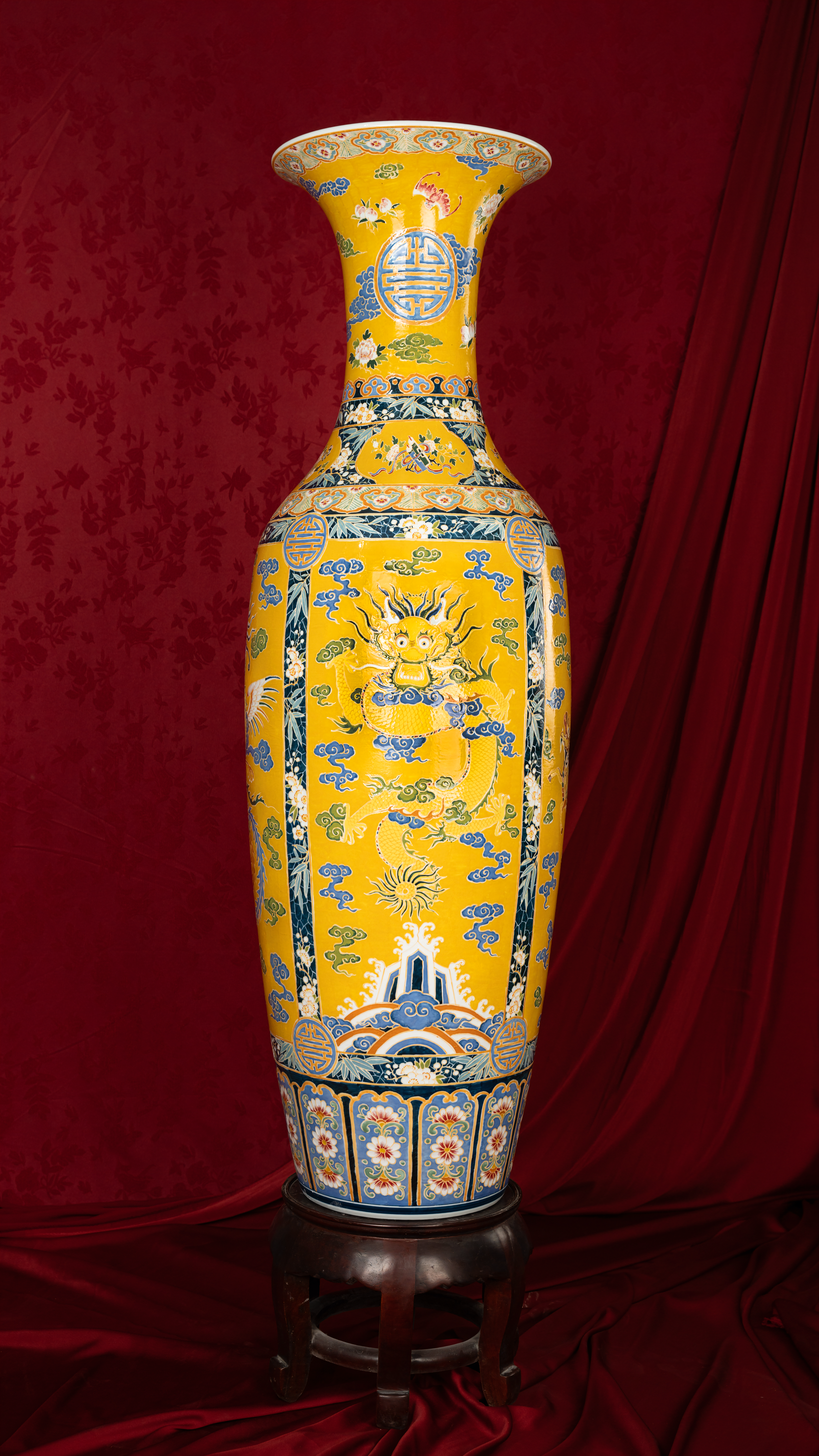 Large decorated Vietnamese vase with intricate dragon motif on a rich red fabric backdrop.