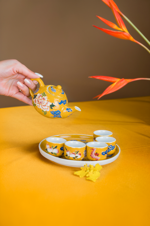 Free A hand pours tea from a yellow floral teapot into matching cups on a vibrant setup. Stock Photo